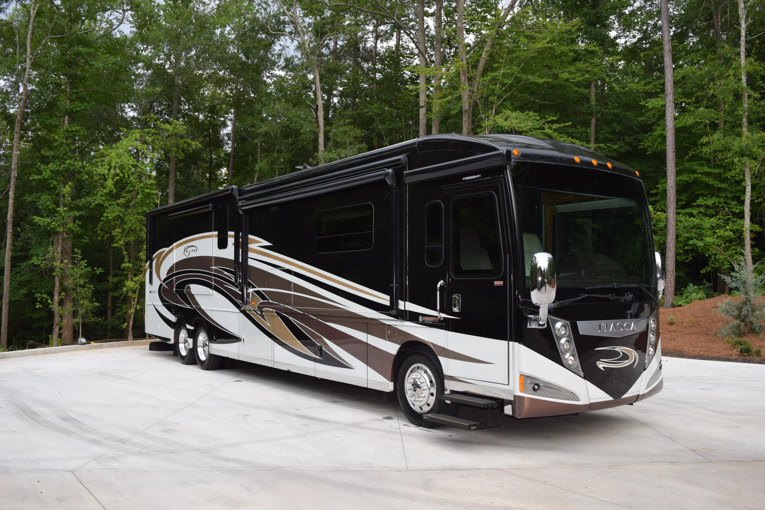 DSC_0521 Black and white motorcoach parked on a concrete surface, surrounded by lush green trees.