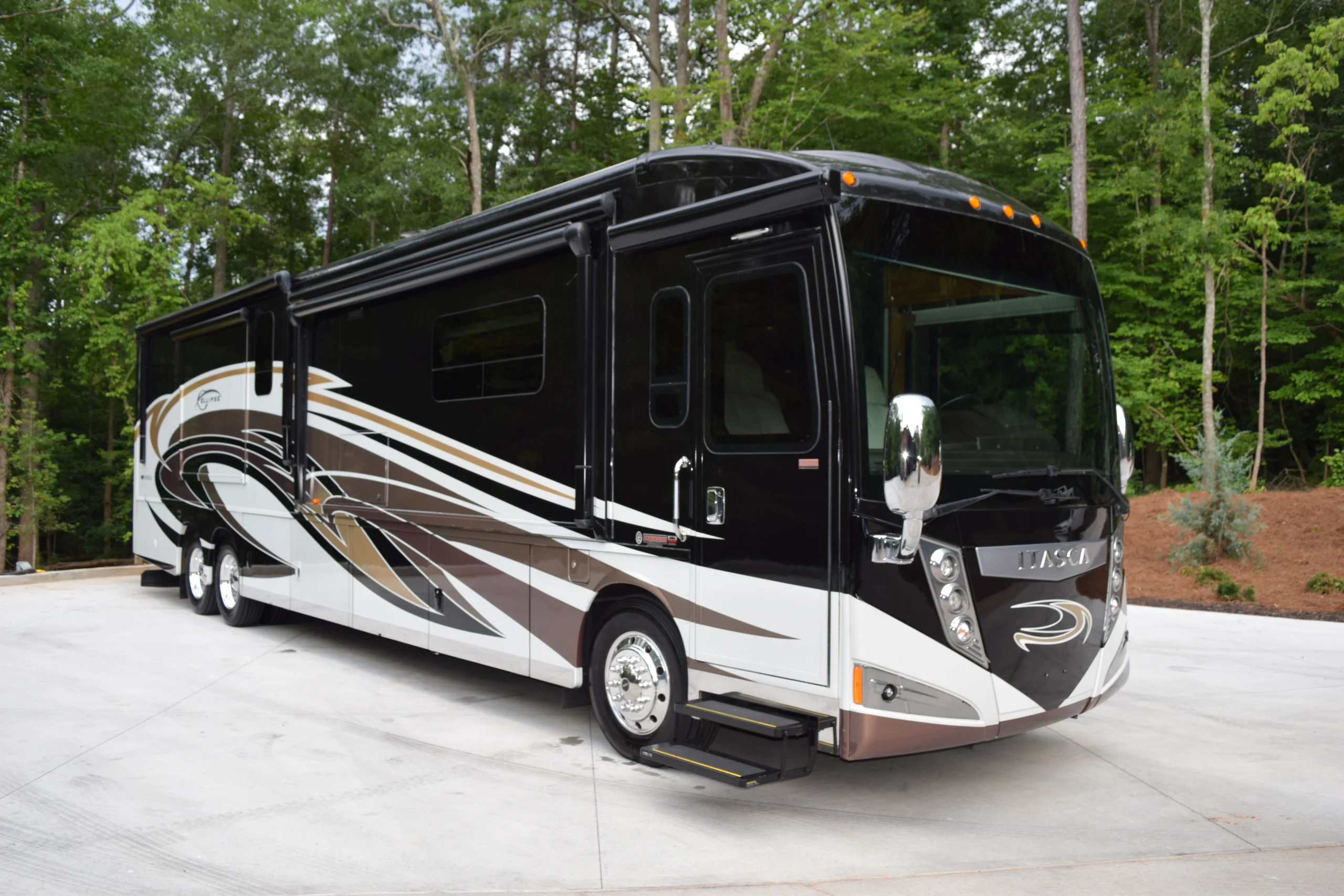 Luxurious black and white motorcoach with sleek design parked on concrete, surrounded by lush green trees.