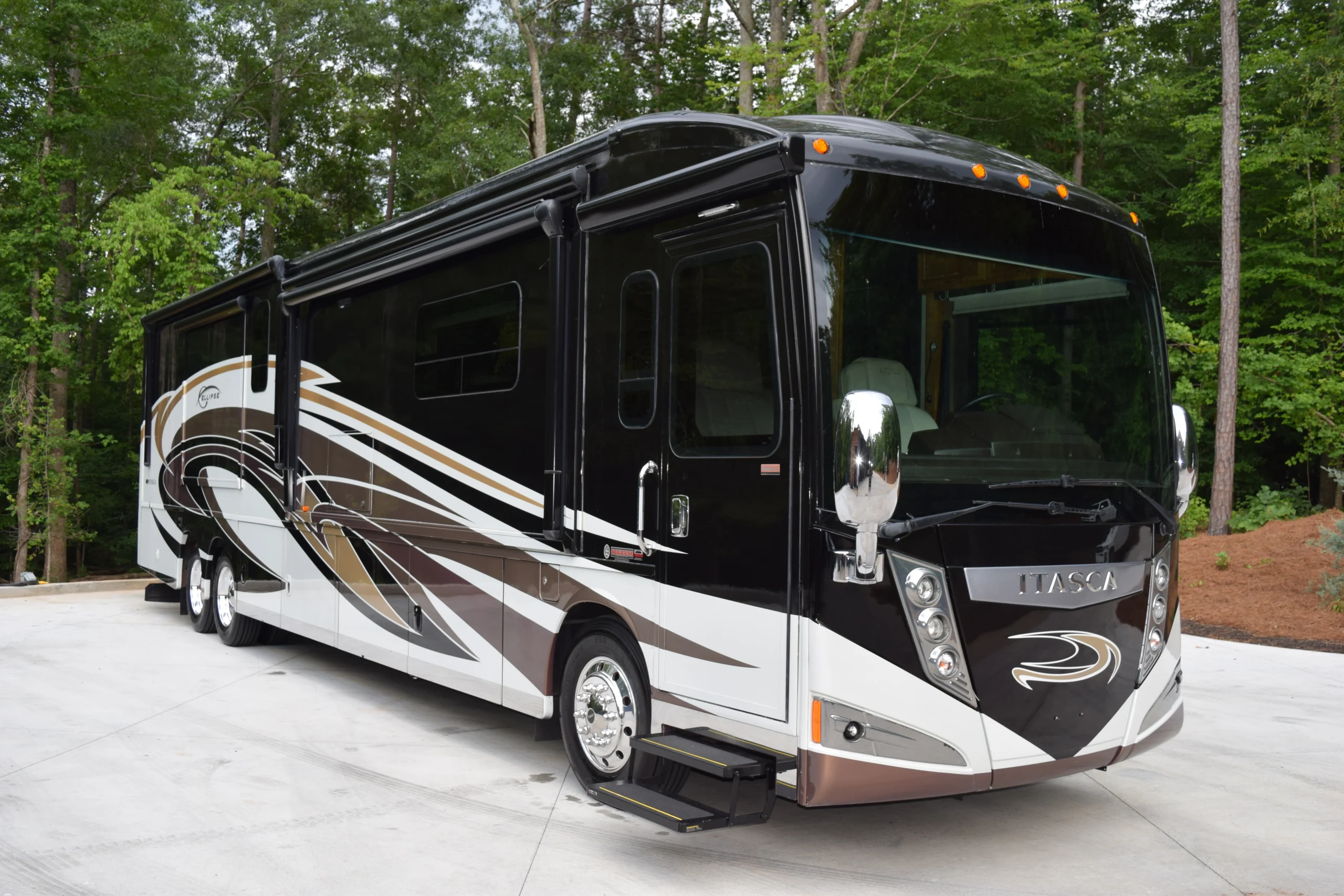 DSC_0523 Luxurious black and white motorcoach with modern graphics parked on a concrete driveway, surrounded by lush green trees.