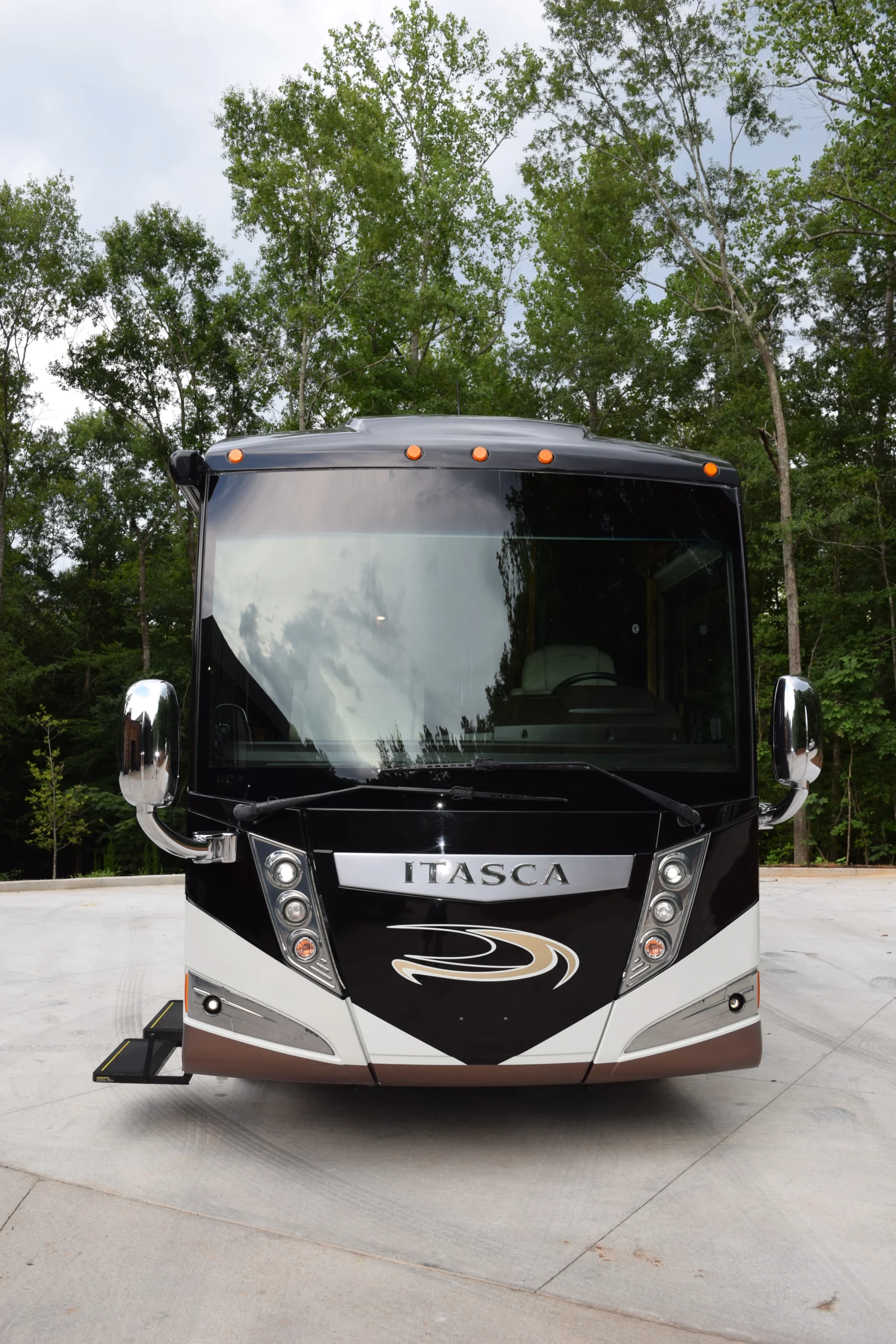 DSC_0525 Front view of black and white Itasca motorcoach surrounded by trees, parked on concrete.
