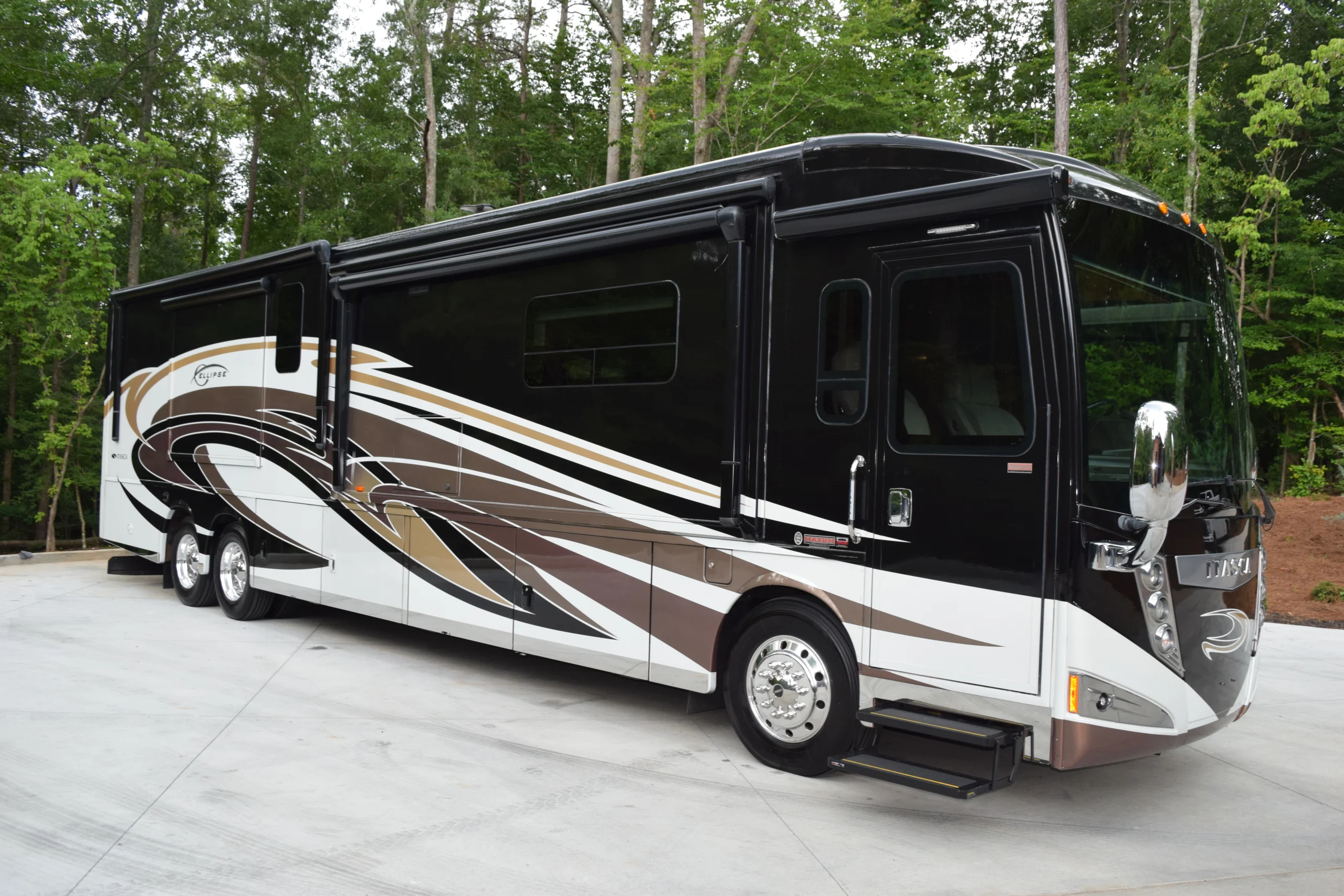 DSC_0536 Luxurious black and white motorcoach parked on a driveway, surrounded by lush green trees.