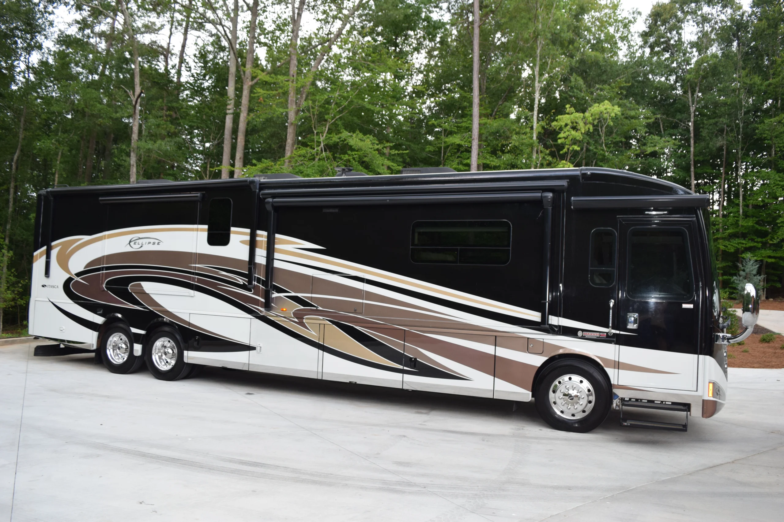 DSC_0537 Luxurious motorcoach RV with brown and white swirl design parked on a concrete pad, surrounded by lush green forest.