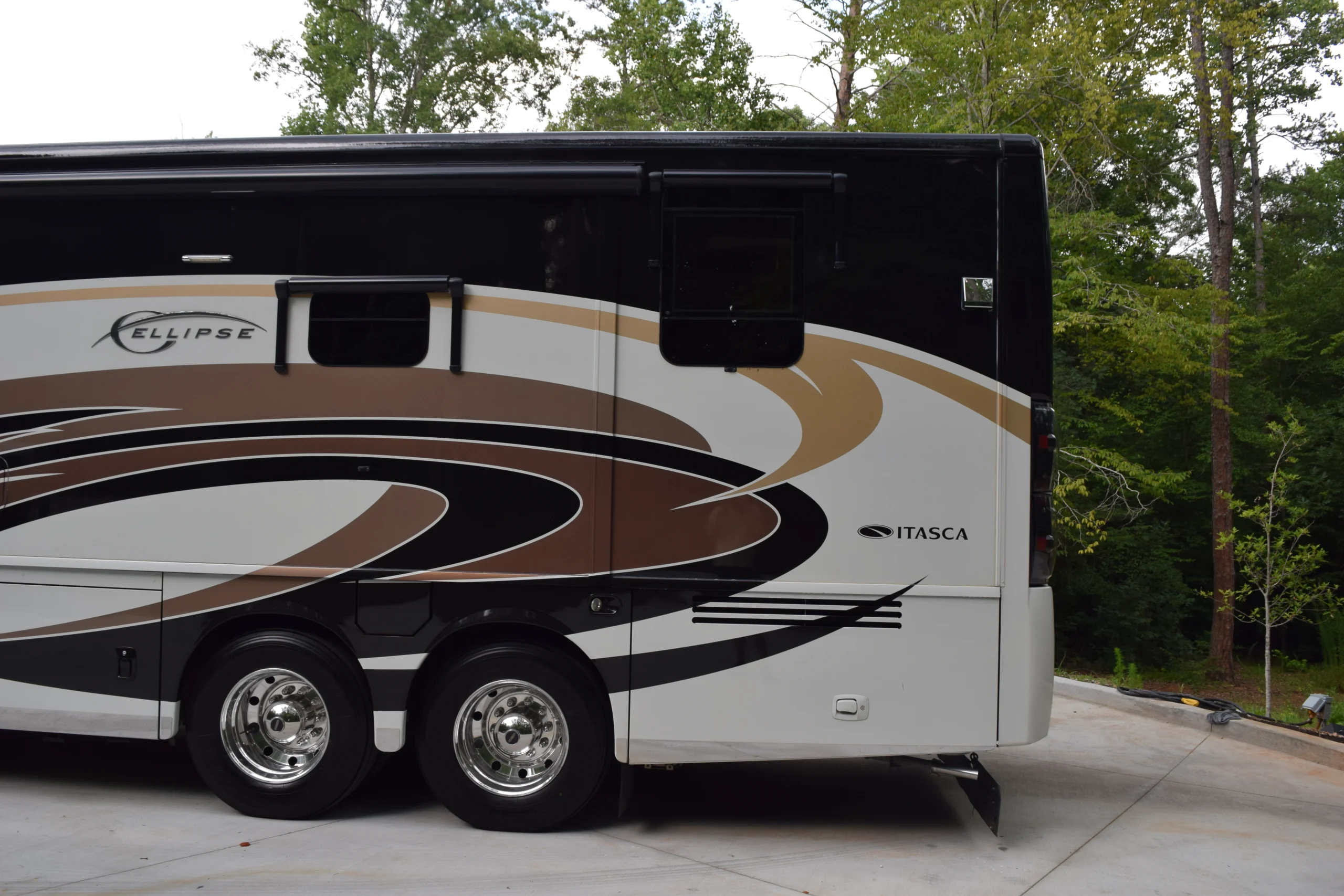 DSC_0539 Luxury Motorcoach with sleek brown and black swirl design parked on a driveway, surrounded by trees.