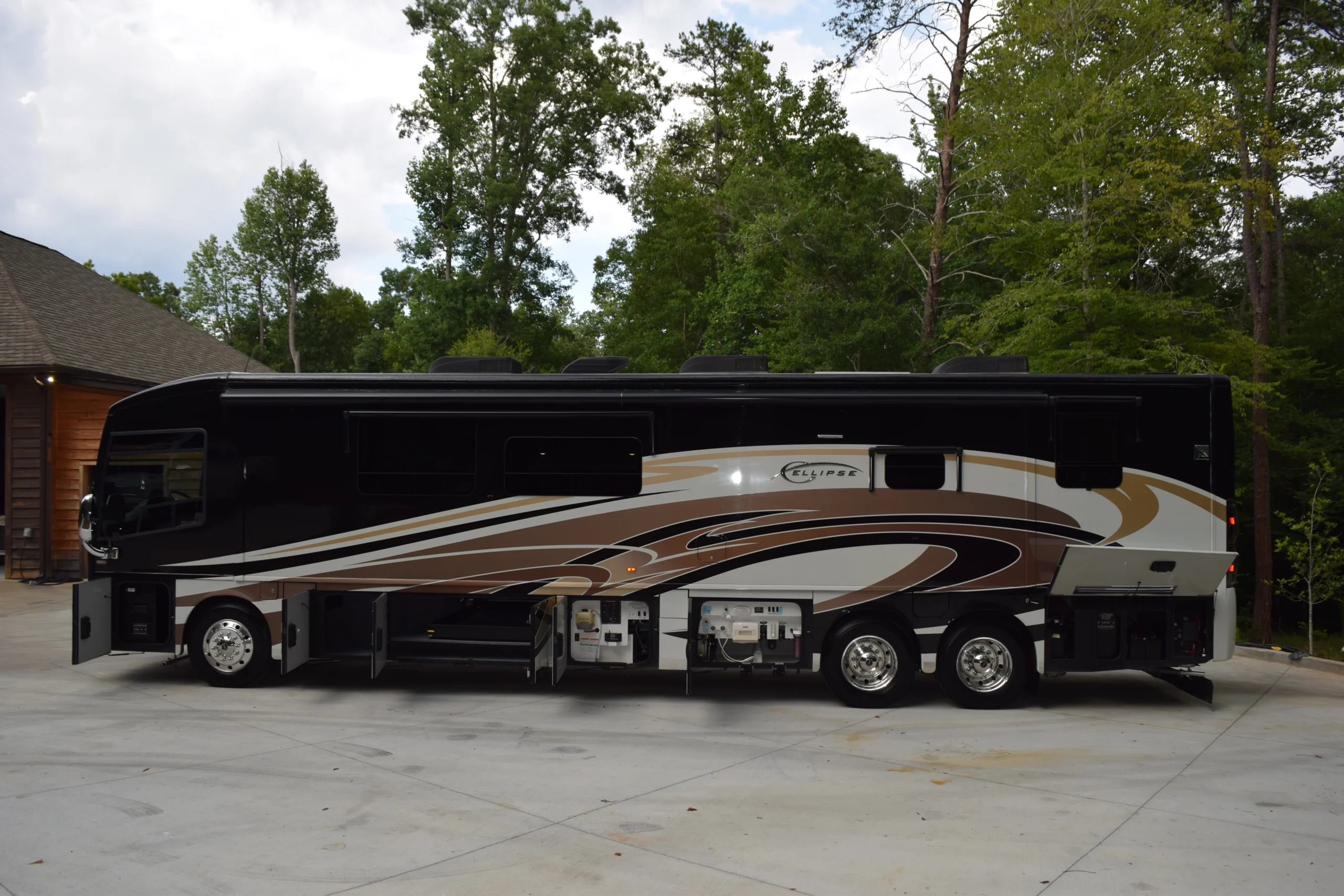 DSC_0544 Luxurious Motorcoach and Rvs parked, surrounded by trees, with open storage compartments and sleek, multicolored design.
