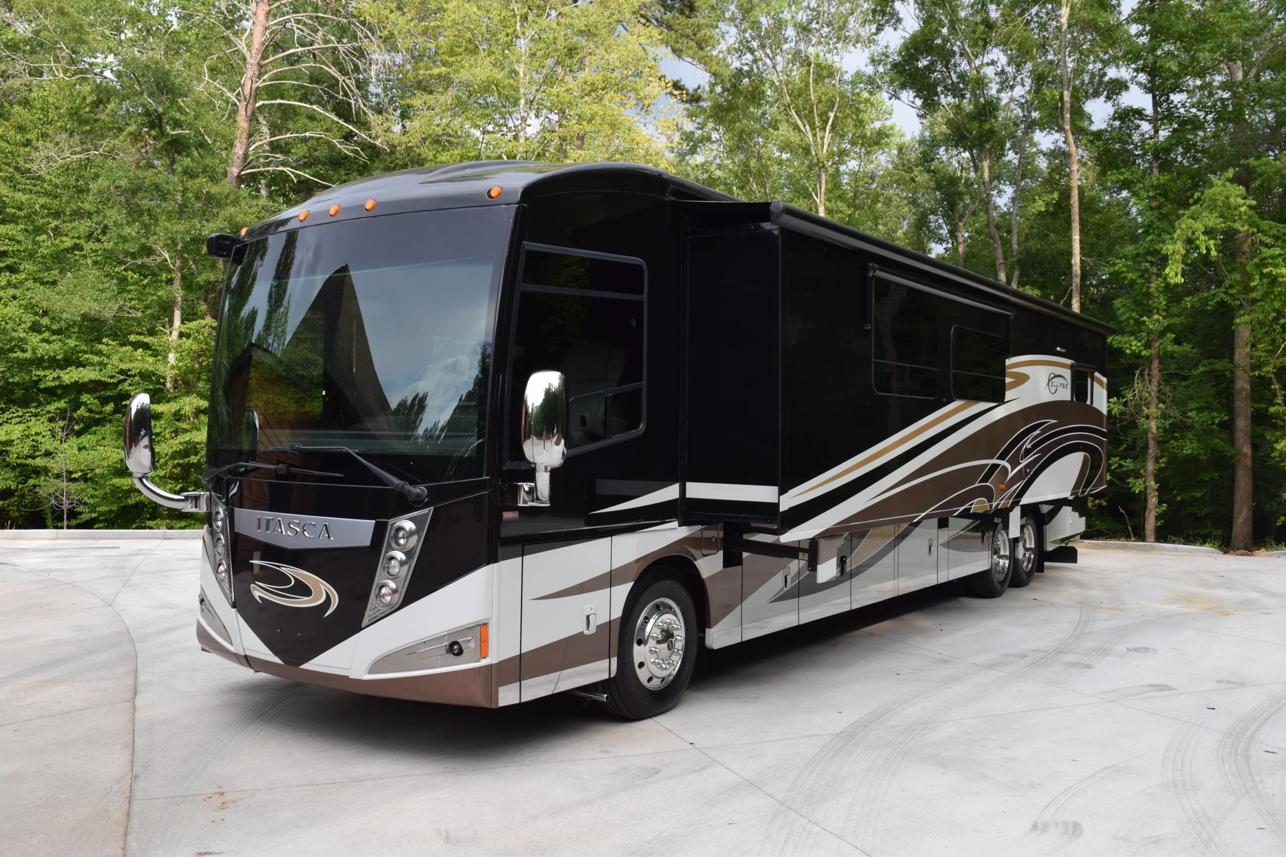 DSC_0548 Luxurious motorcoach with sleek black and silver design parked on concrete, surrounded by lush green trees.