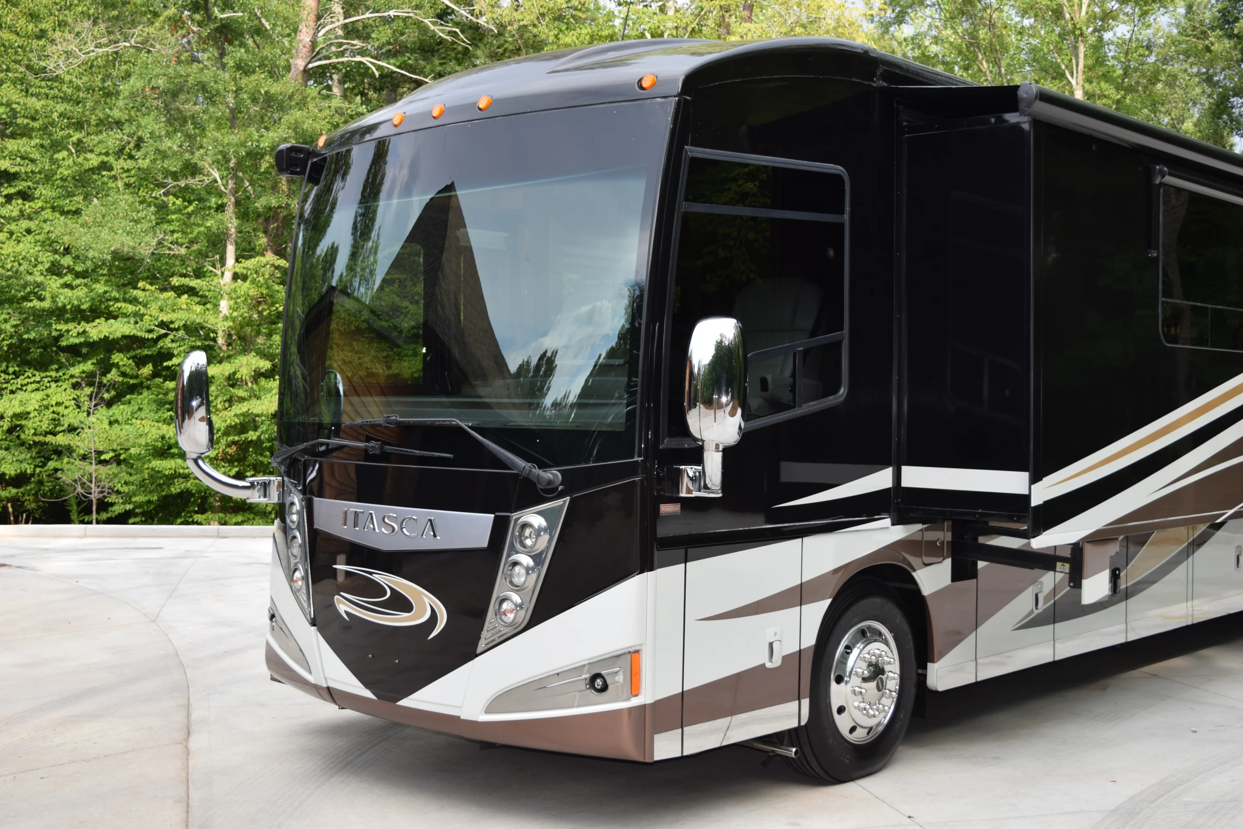 DSC_0549 Luxurious black and white motorcoach parked in a lush, wooded area, showcasing sleek design and large side mirrors.