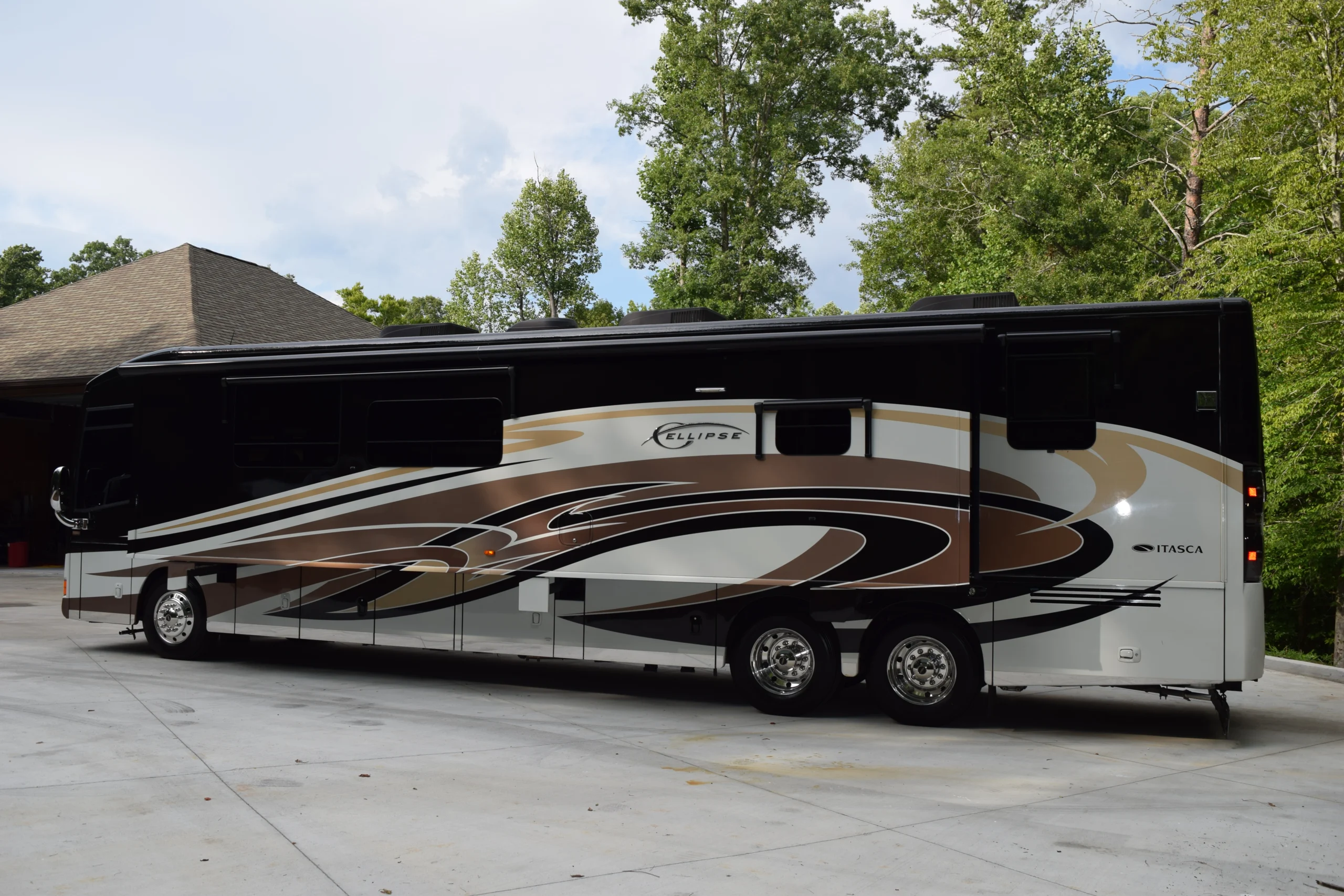 DSC_0551 Large, sleek motorcoach with brown, black, and white swirl designs parked outdoors, surrounded by trees.