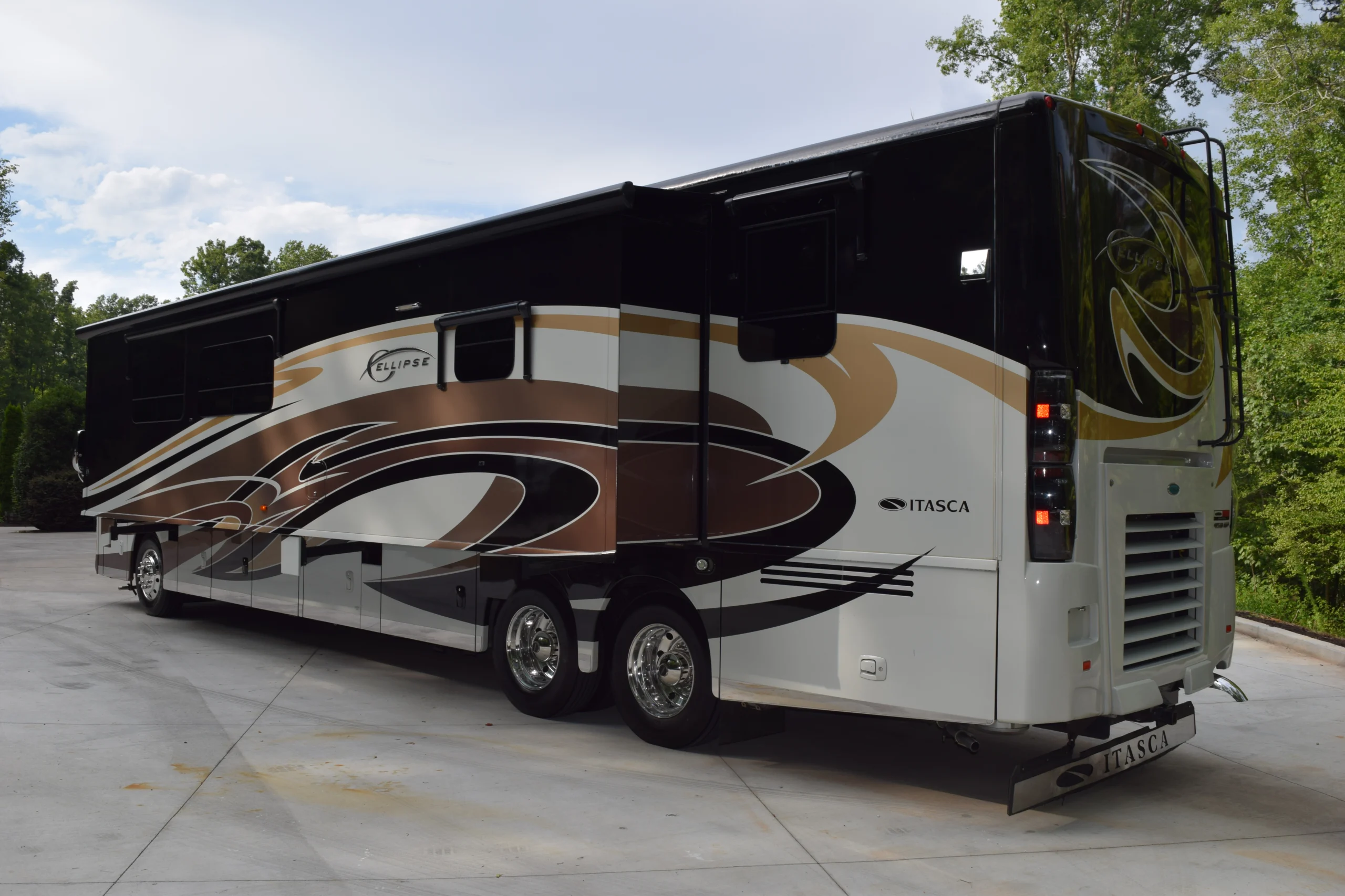 DSC_0552 Luxurious motorcoach with sleek black and tan design parked on a driveway, surrounded by greenery.