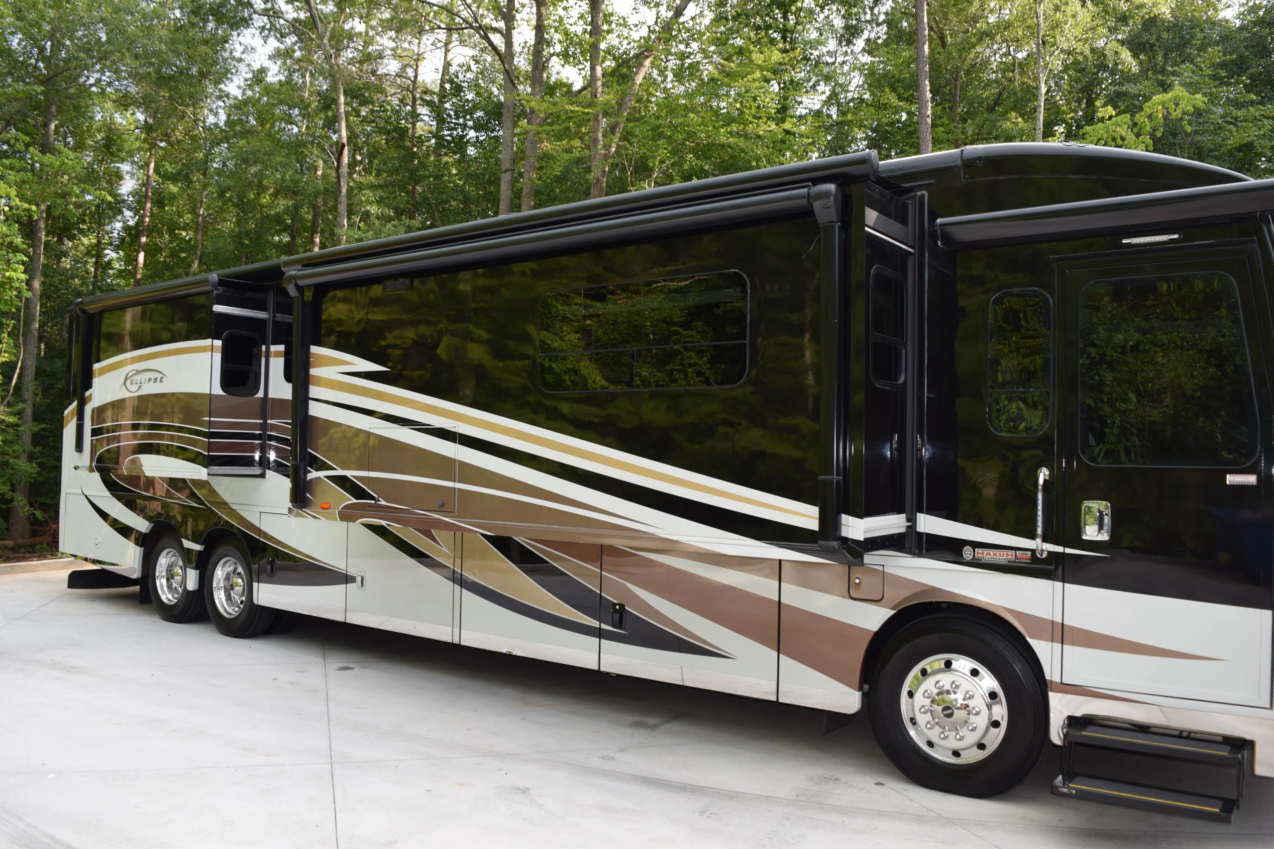 DSC_0553 Luxurious motorcoach with brown and white swirls, parked on a paved surface against a forested backdrop.