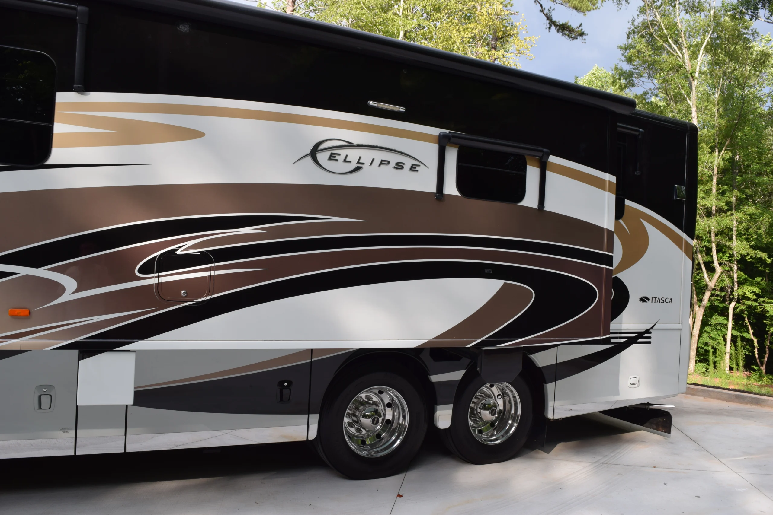 DSC_0558 Side view of a luxury RV featuring sleek brown and gold swirls. Shiny dual wheel set. Keywords: Motorcoach and RVs.