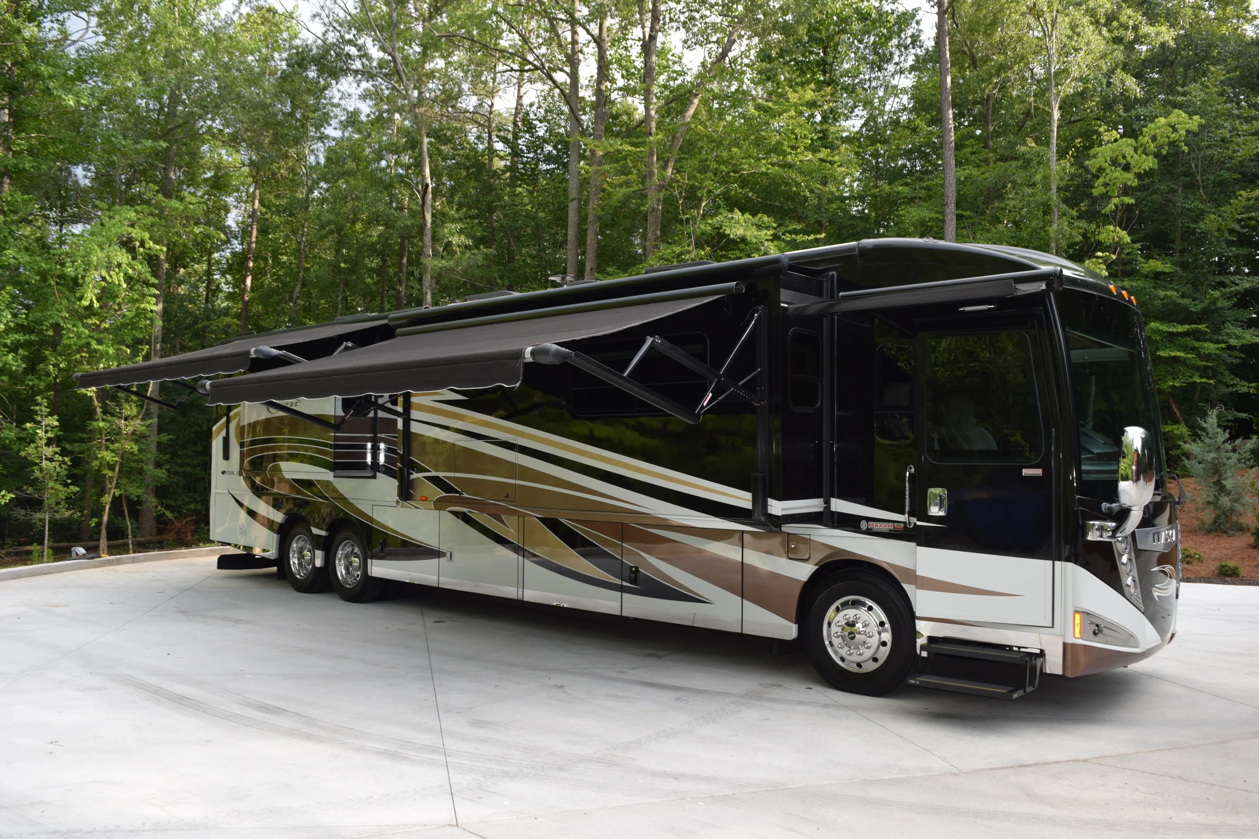 DSC_0559 Luxurious Motorcoach and RV with extended awning parked on concrete amidst lush green trees.