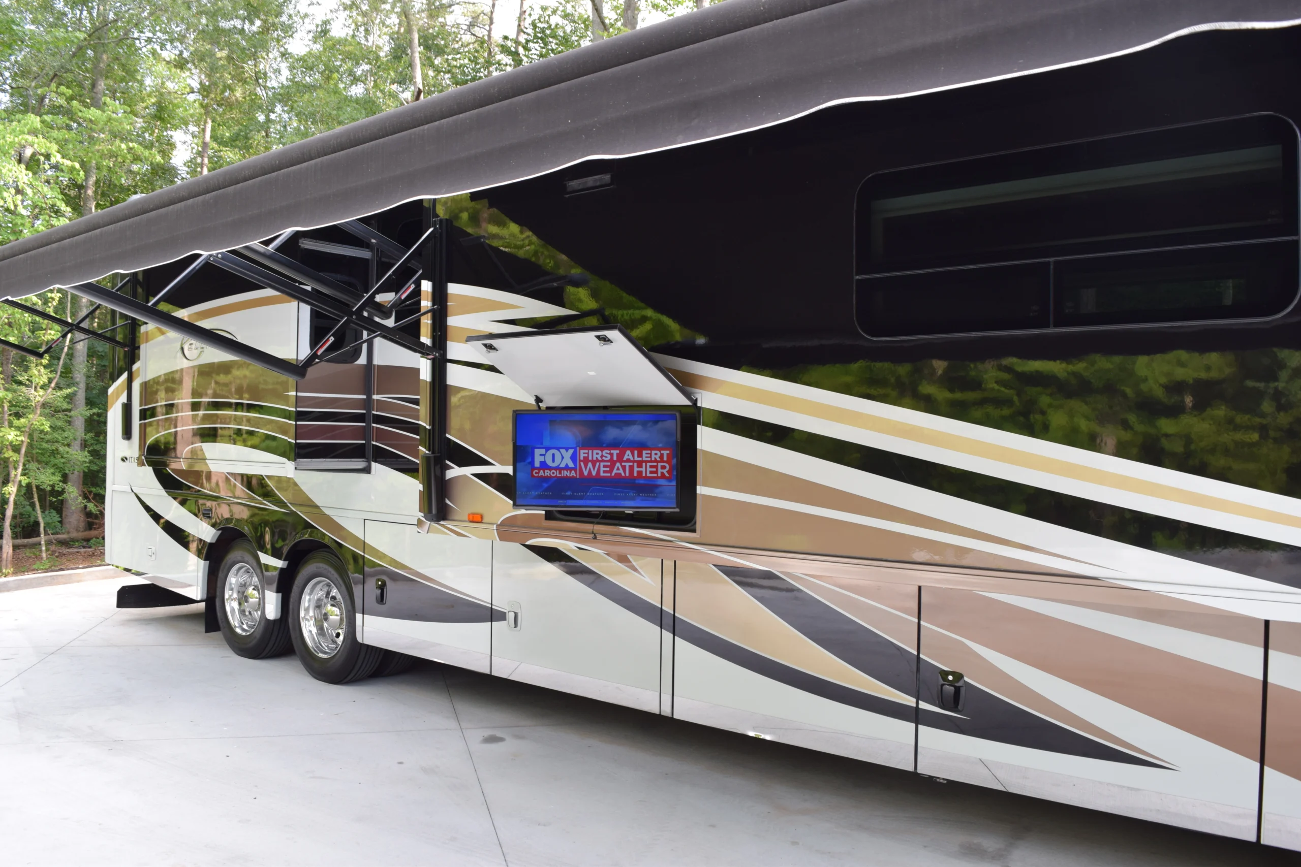 DSC_0563 Luxurious RV with extended awning, outdoor TV showing Fox Carolina weather alert. Ideal for Motorcoach and Rvs enthusiasts parked in wooded area.