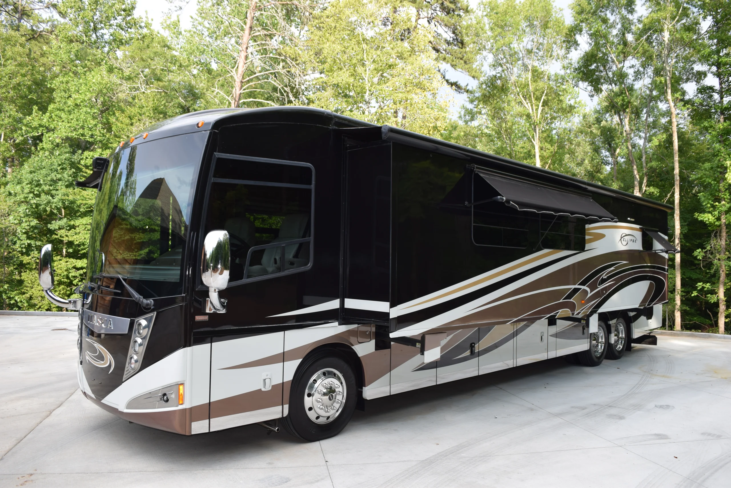 DSC_0566 Luxury motorcoach with sleek black and white design parked on concrete, surrounded by lush green trees.