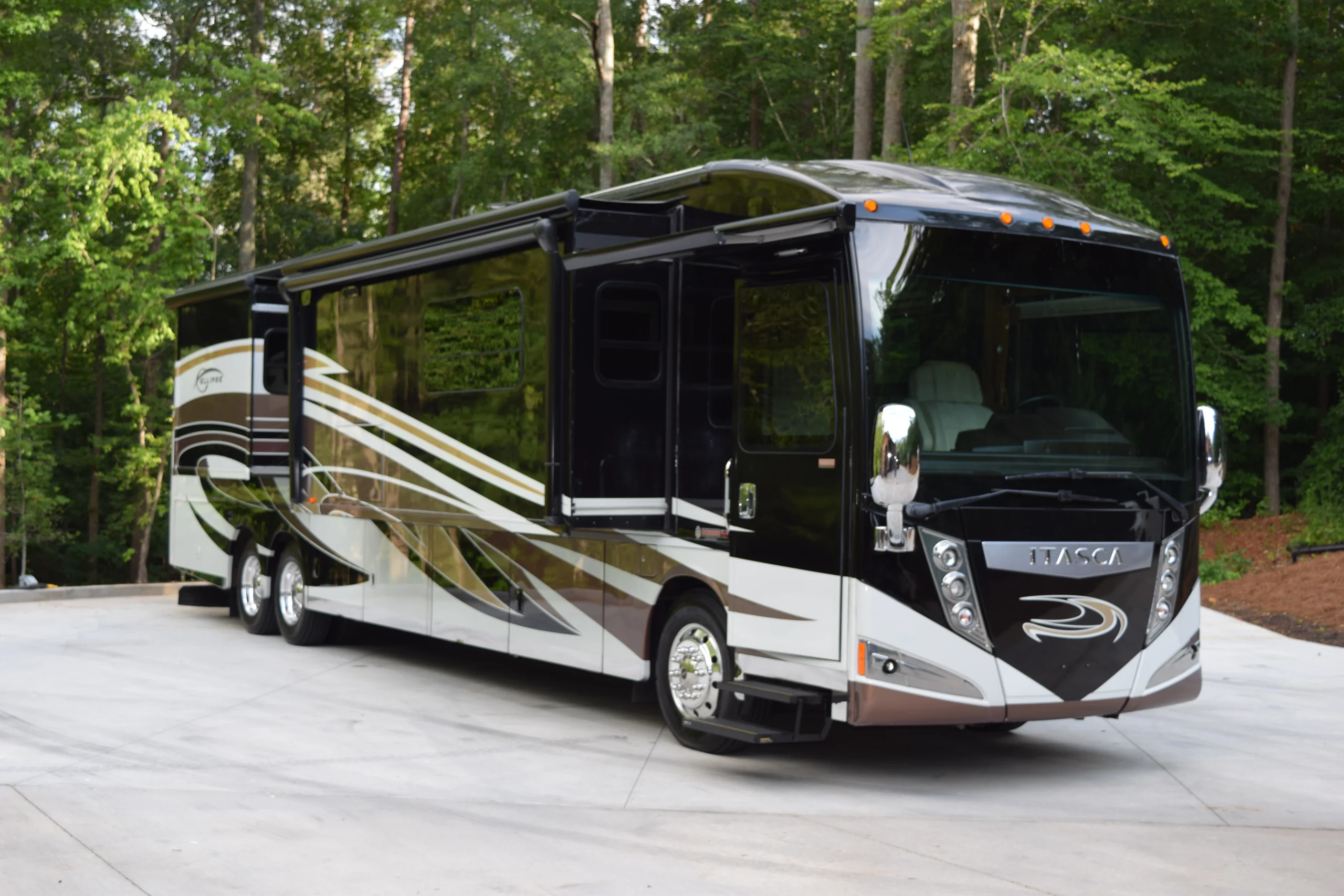 DSC_0572 Luxurious black and white motorcoach parked on a concrete pad, surrounded by lush green trees.