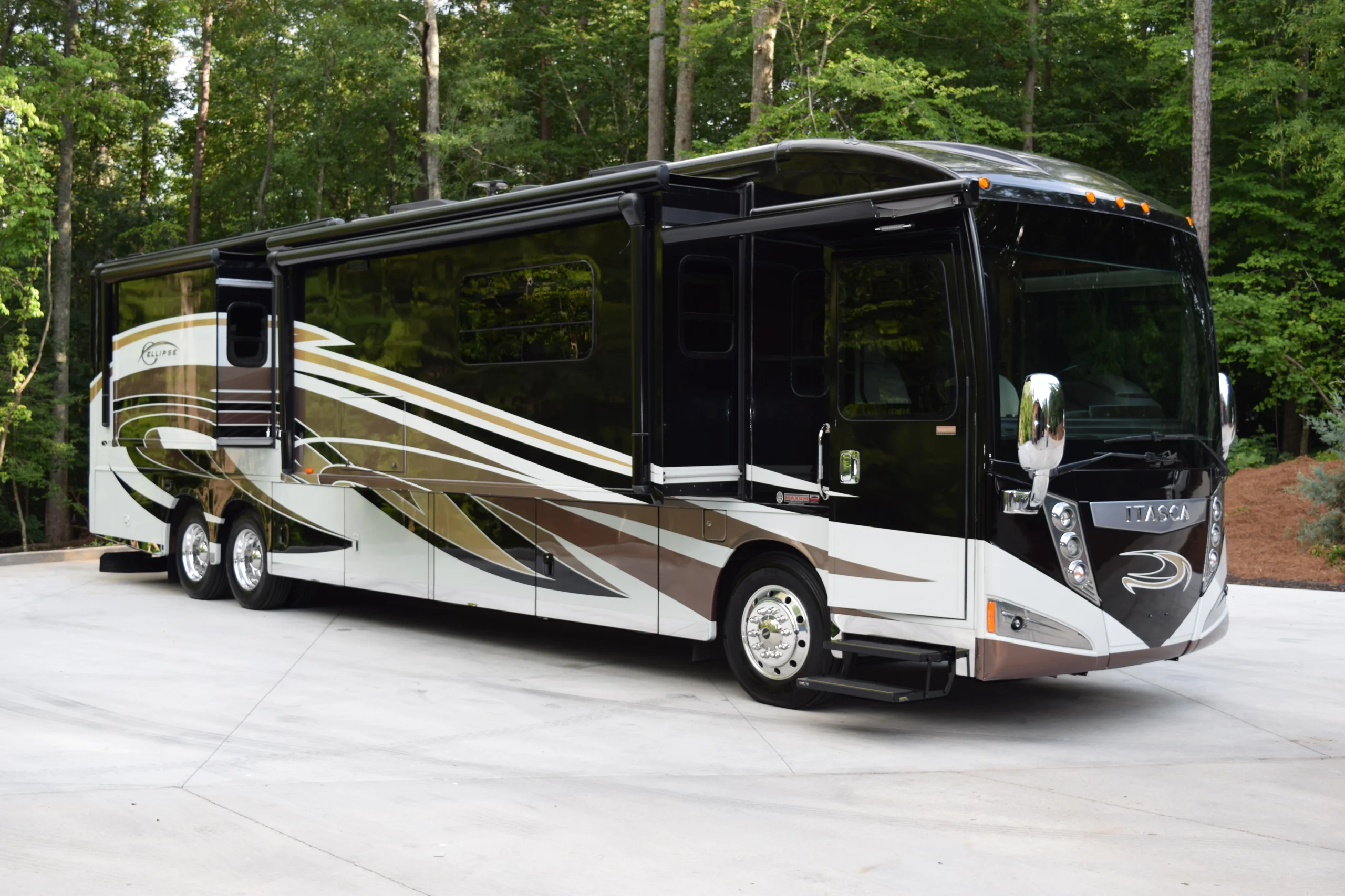 DSC_0573 Luxury motorcoach parked on concrete with a sleek design, surrounded by trees, showcasing elegant black, white, and gold patterns.