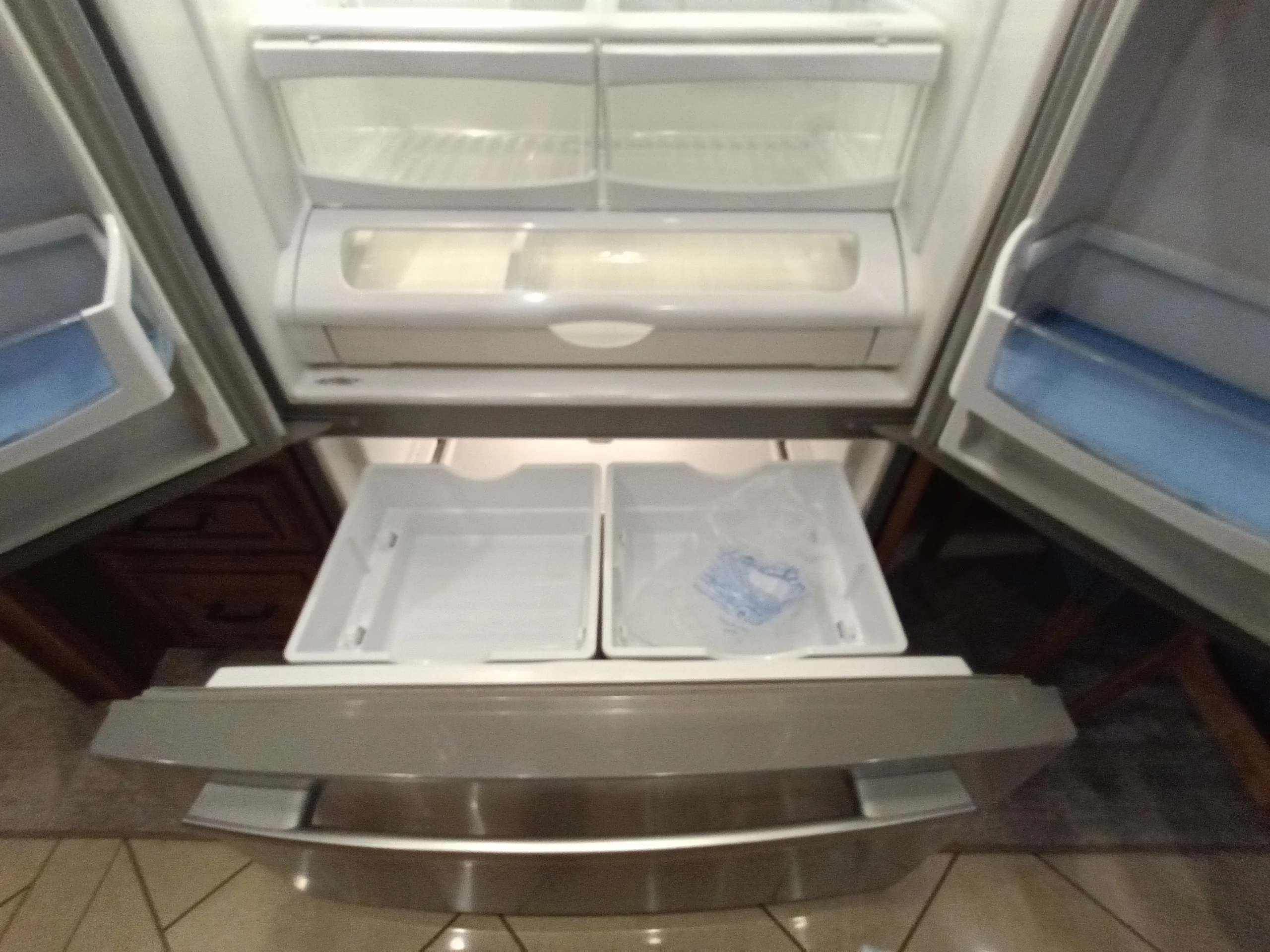 IMG_20260710_172421_287 Open stainless steel French door refrigerator with empty compartments and a clear plastic bag, commonly found in Motorcoach and RVs.