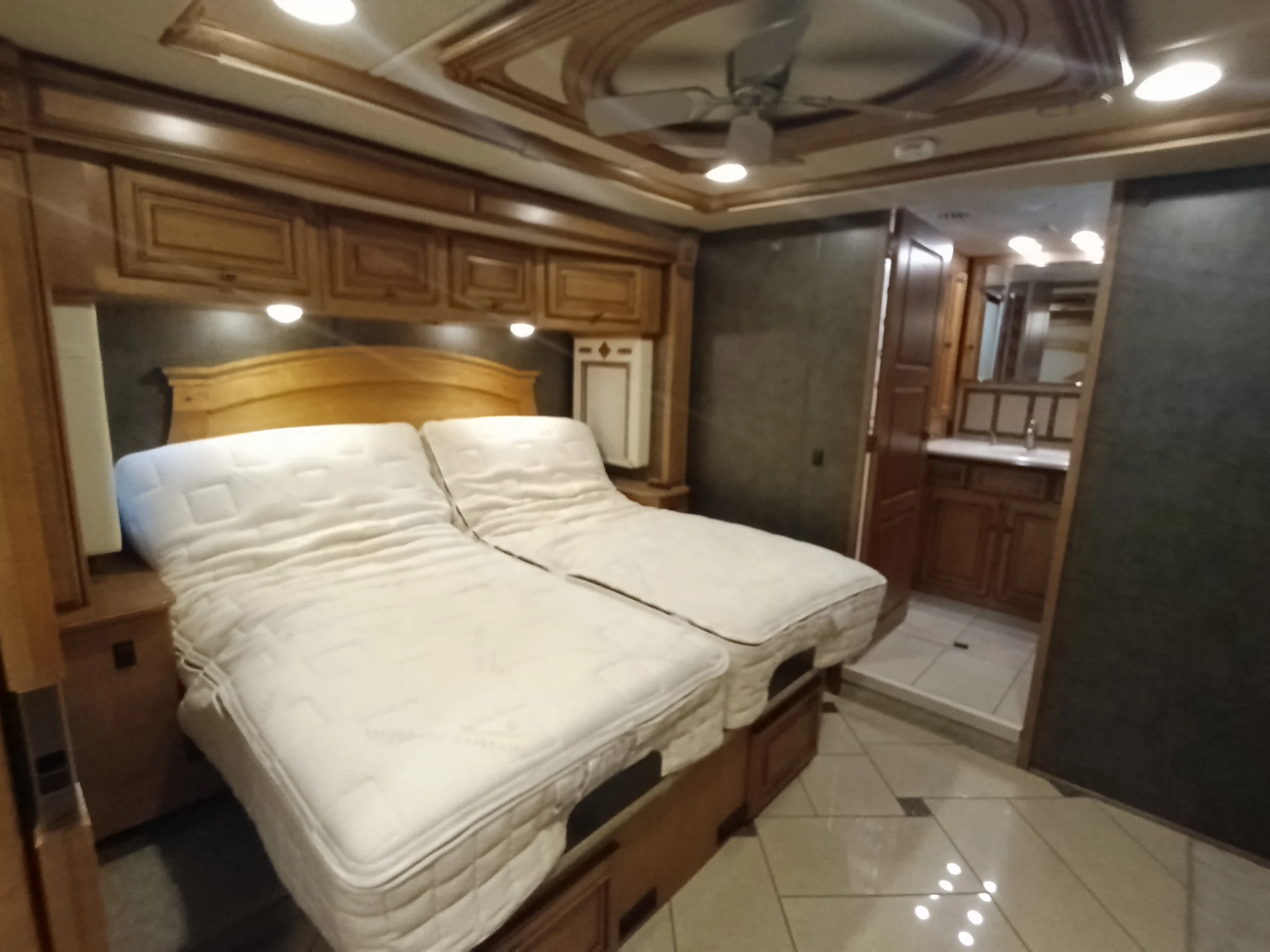 IMG_20260710_172551_555 Luxurious Motorcoach and RVs bedroom with two adjustable beds, wooden cabinets, and a view into a spacious bathroom.