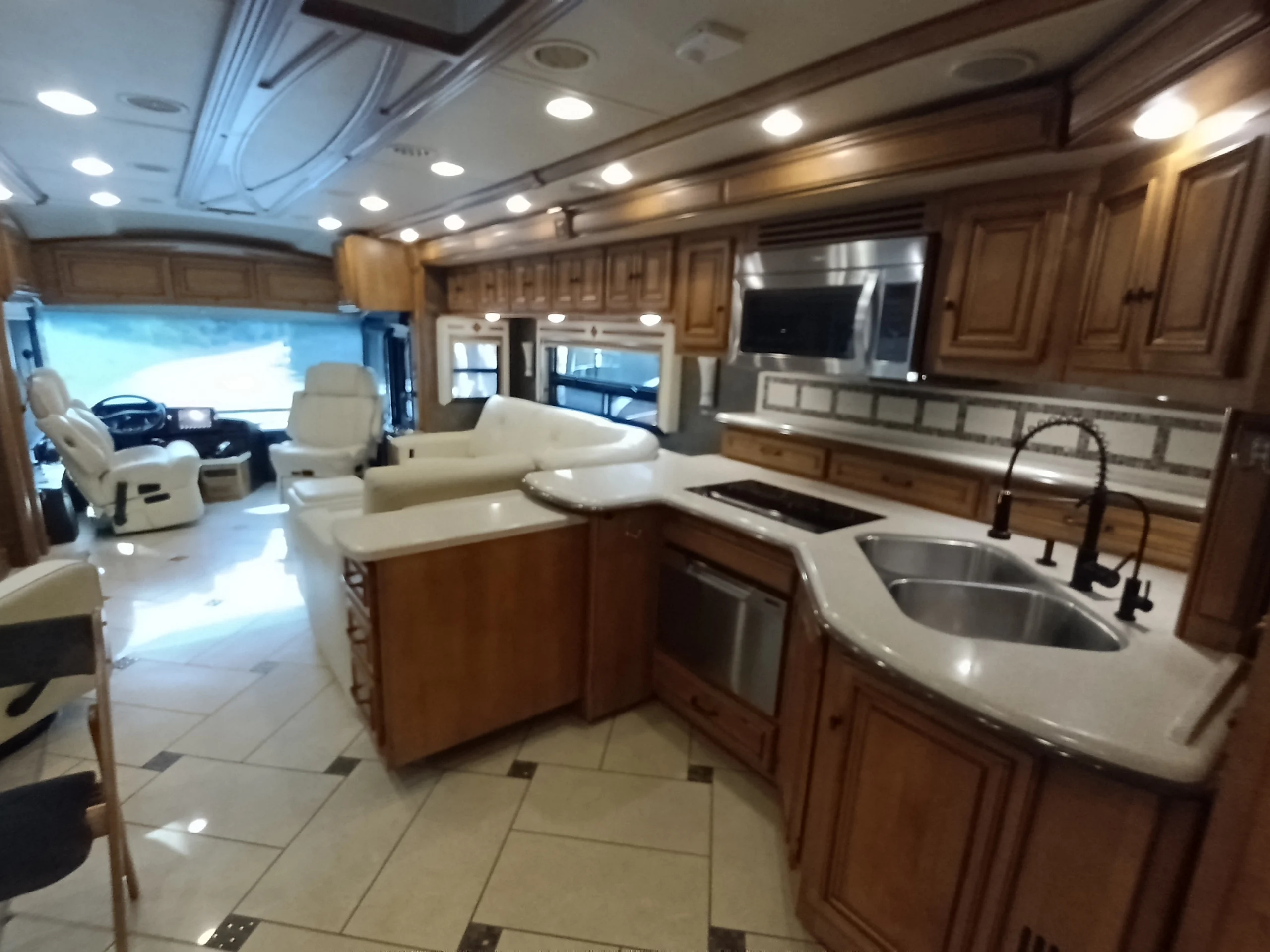 IMG_20260710_172804_061 Spacious motorcoach interior featuring a modern kitchen with wood cabinets, seating area, and driver's cockpit at the front.