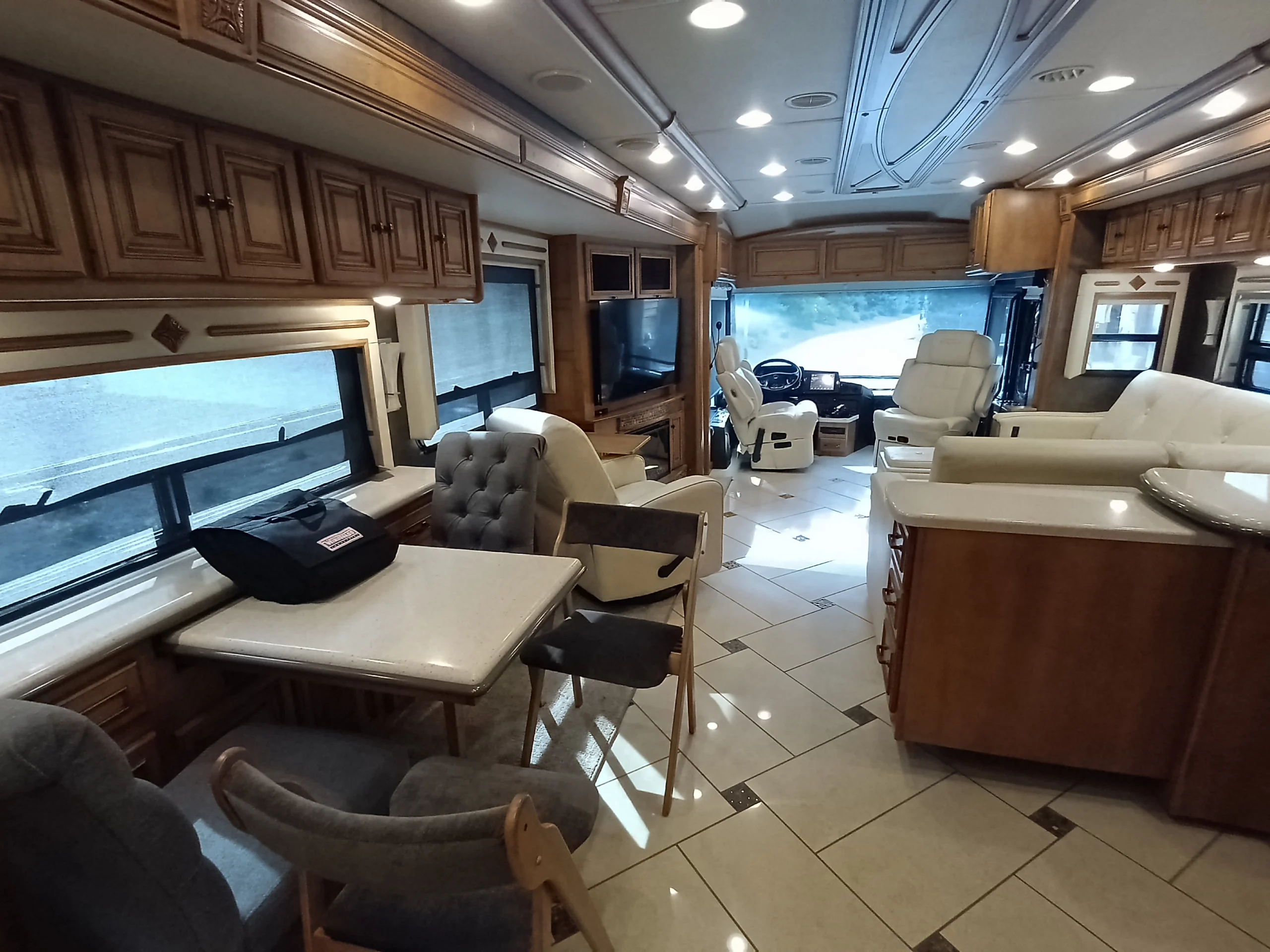 IMG_20260710_172809_815 Spacious Motorcoach interior with leather seating, dining area, tiled floor, and wood cabinets, combining comfort and functionality.