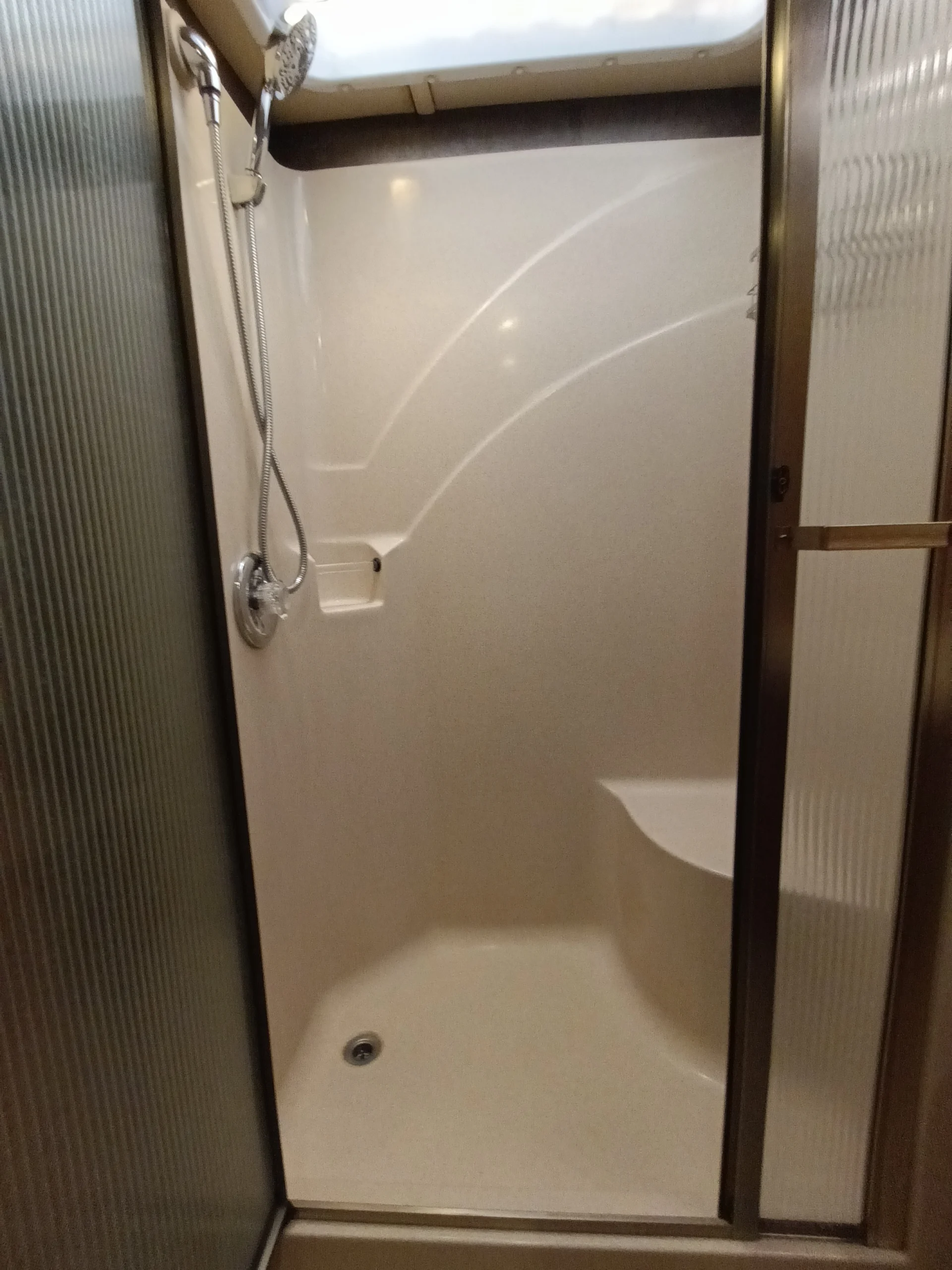 IMG_20260710_172939_546 Compact RV shower with handheld showerhead, skylight, and frosted glass door, typical in motorcoaches and RVs.