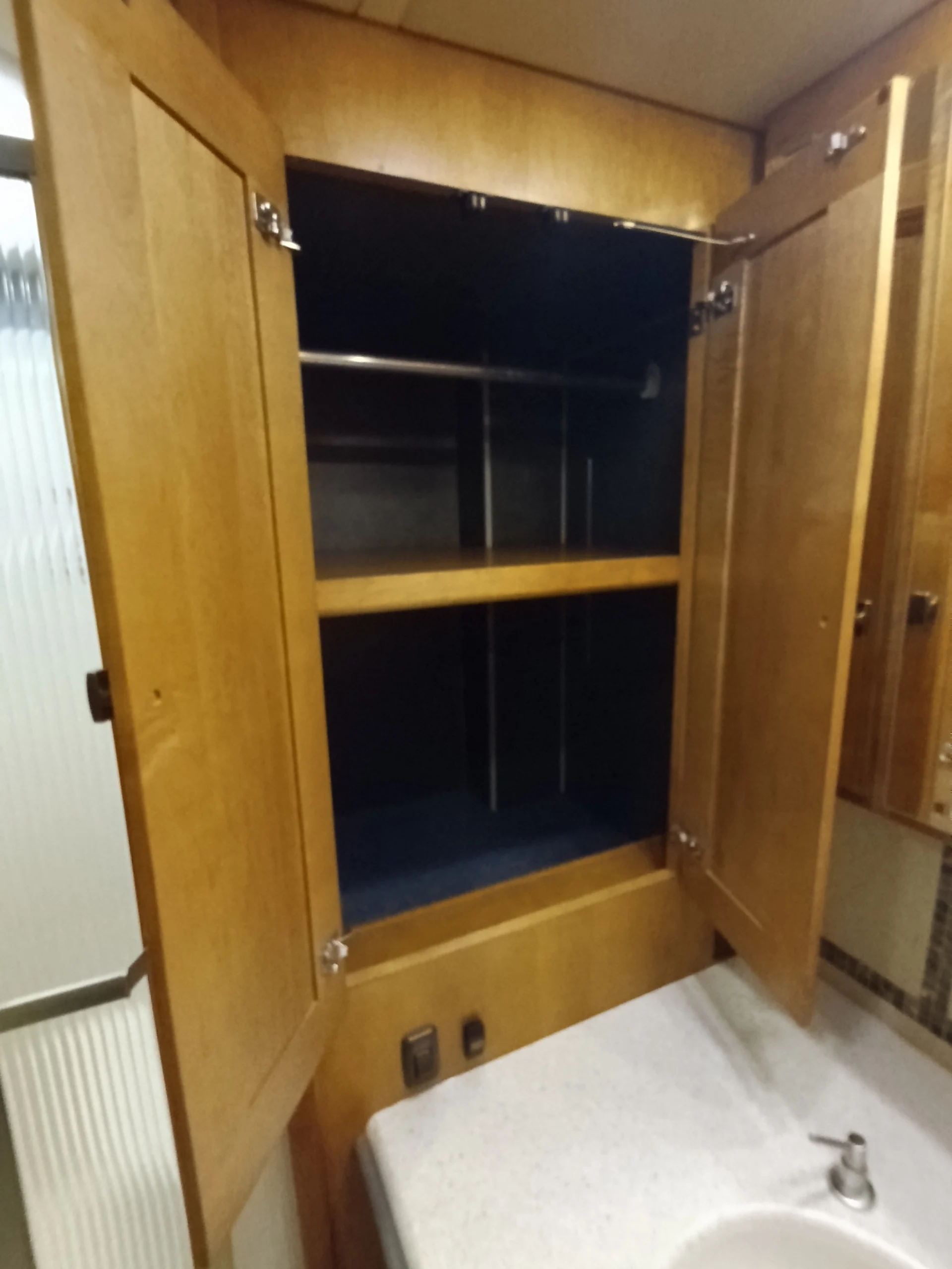 IMG_20260710_172953_453 Open wooden cabinet above a countertop with a sink, suitable for Motorcoach and RVs, showcasing spacious shelves and storage.