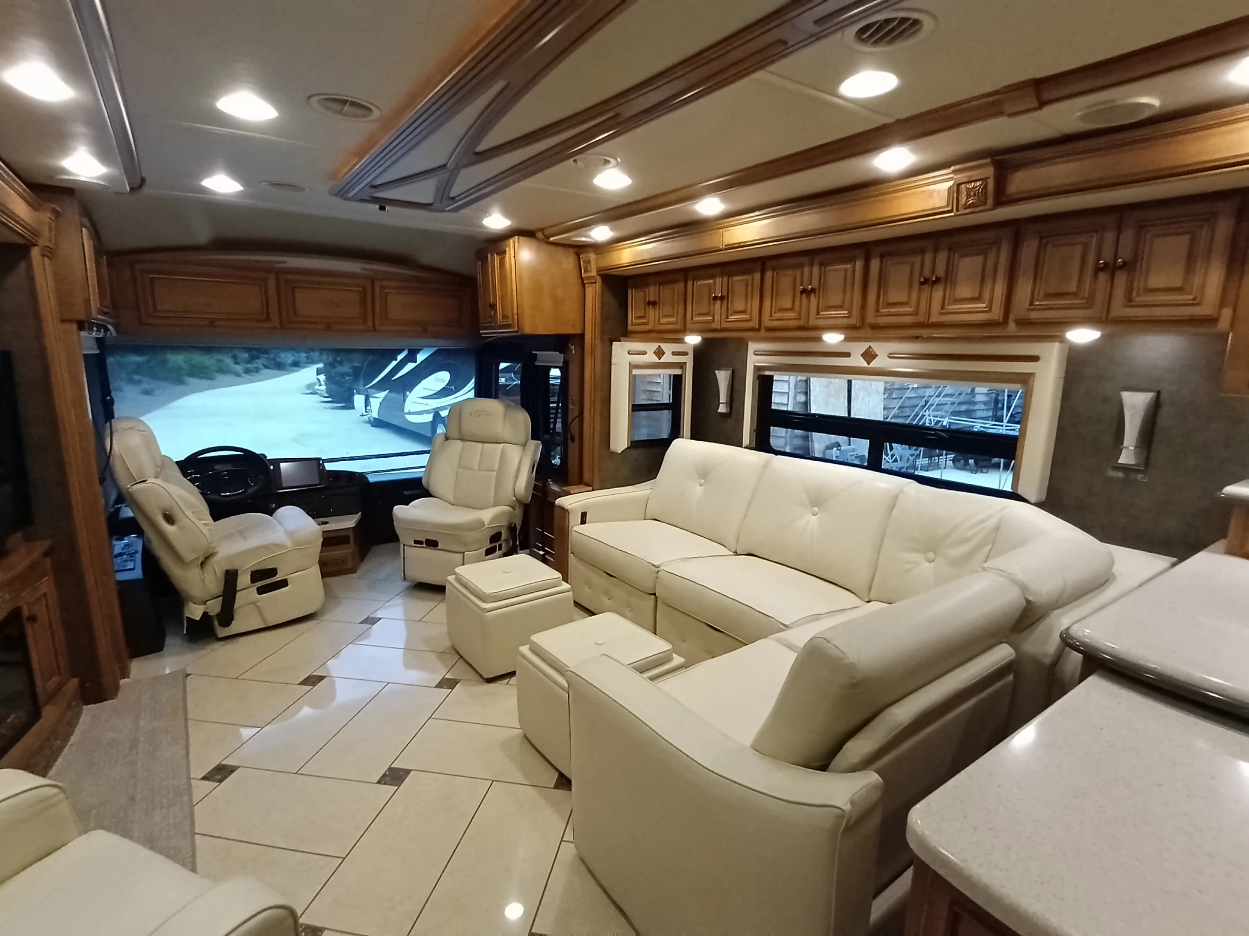 IMG_20260710_174837_190 Luxurious motorcoach interior with plush white seating, tiled floor, wooden cabinets, and a view through the windshield.