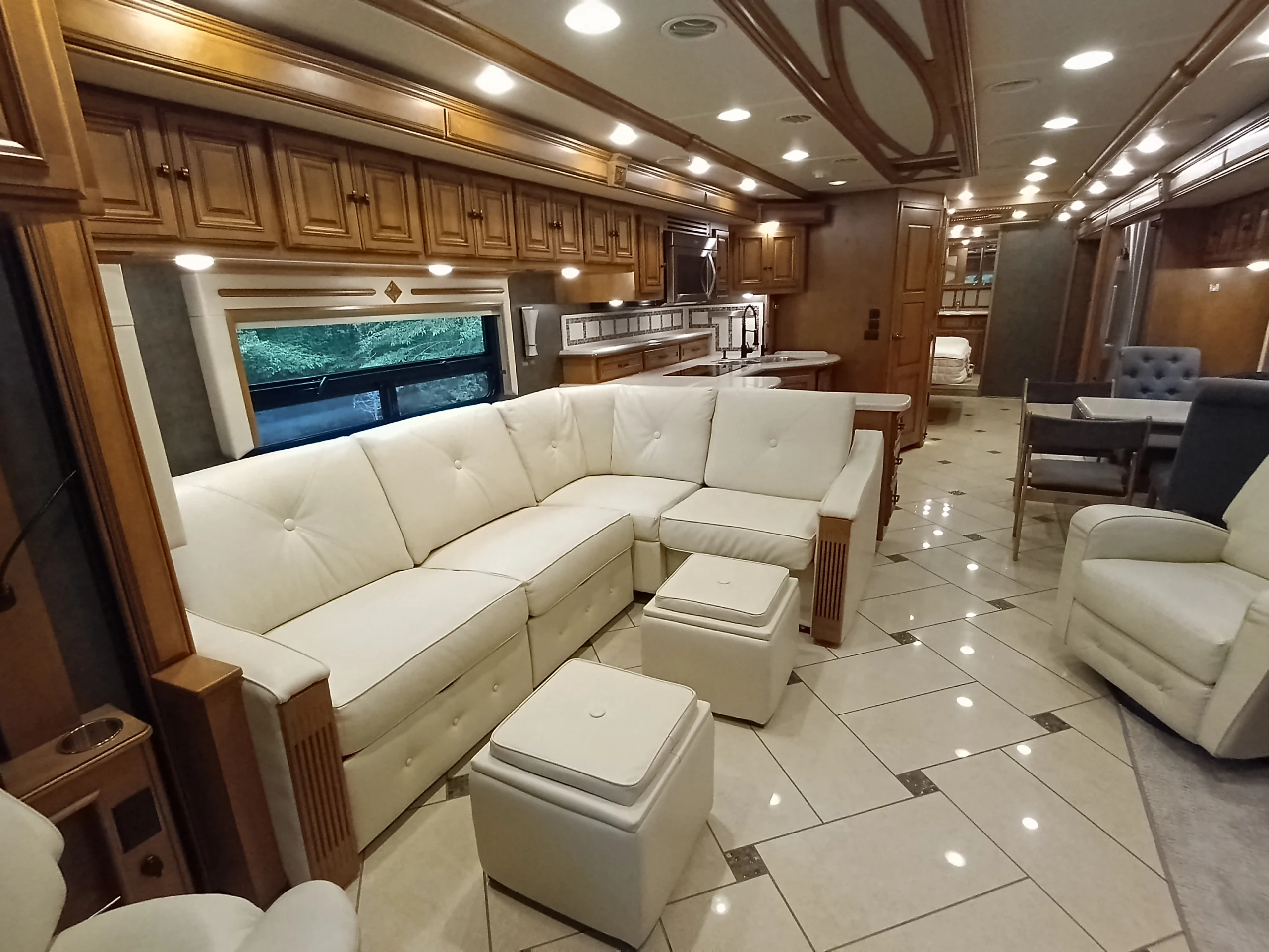 IMG_20260710_175035_476 Luxurious motorcoach interior featuring white sectional sofa, elegant wood cabinetry, tiled floor, and a dining area with upholstered chairs.