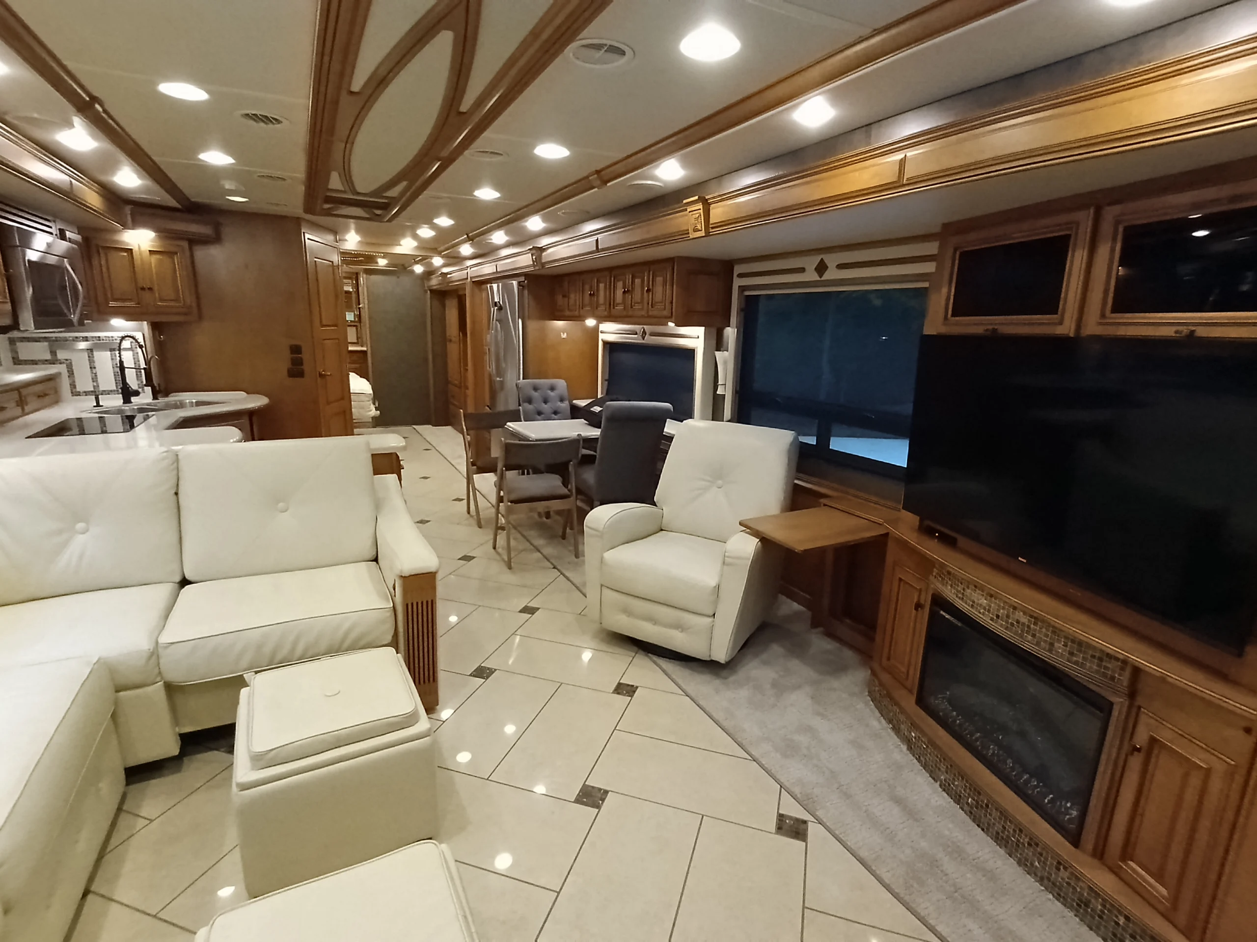 IMG_20260710_175041_735 Luxurious motorcoach interior with plush seating, modern kitchen, dining area, TV, and fireplace, surrounded by wood finishings.