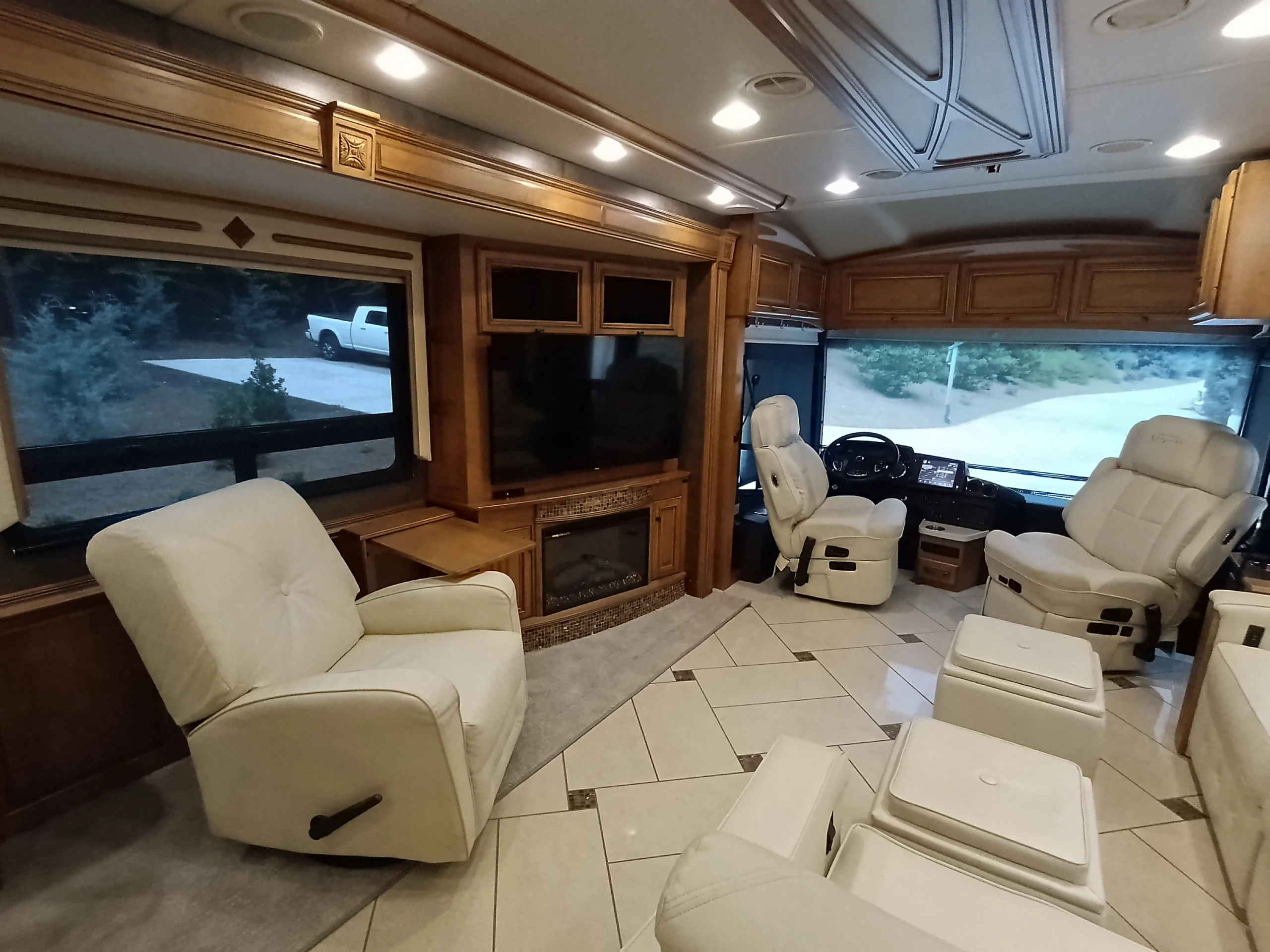 IMG_20260710_175144_093 Luxurious motorcoach interior with cream leather chairs, large windows, wood paneling, and a flat-screen TV. Comfortable driving and lounging area.