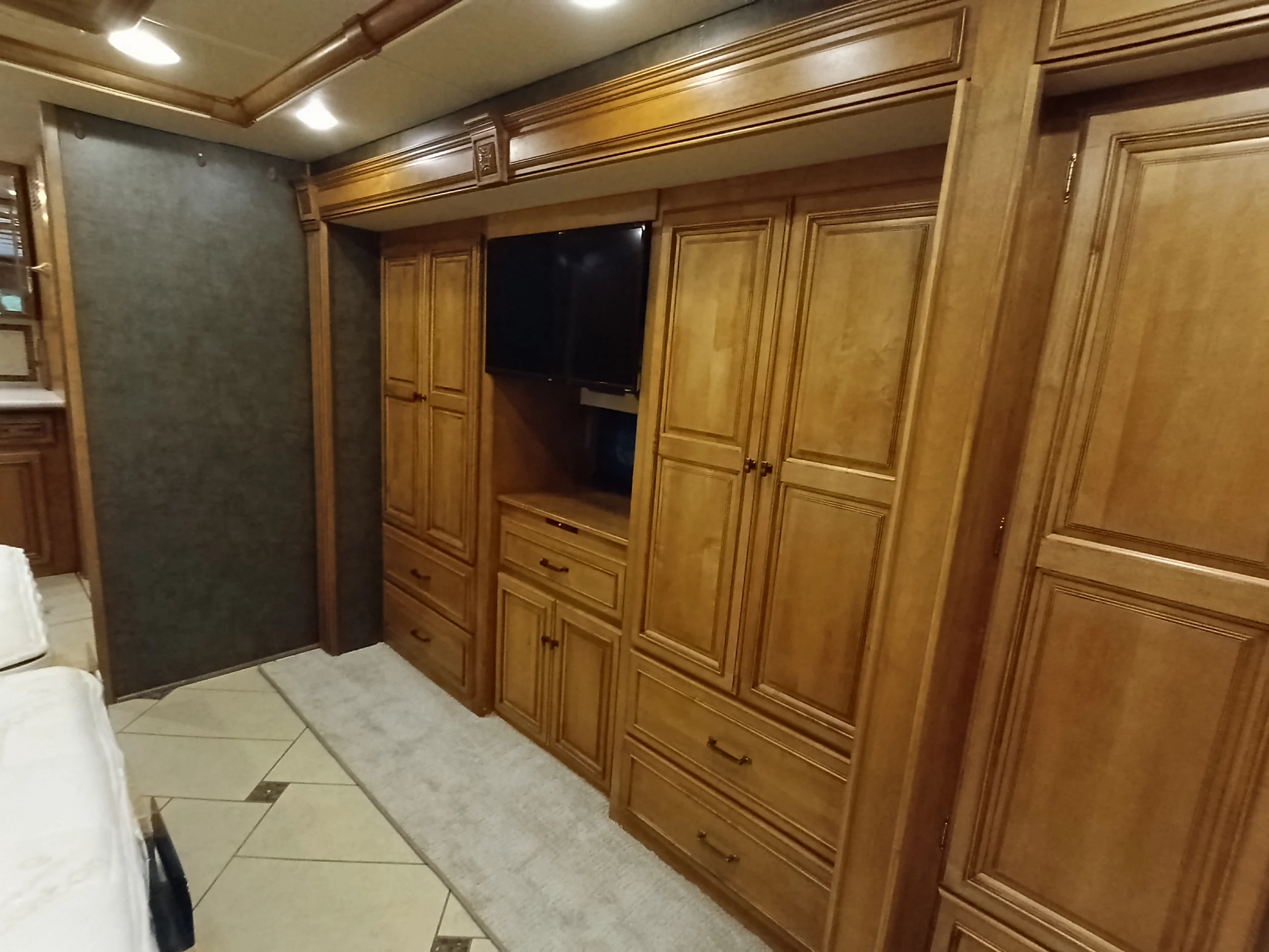 IMG_20260710_175203_881 Wooden cabinetry lining the wall of a motorcoach interior, with a TV and ample storage.