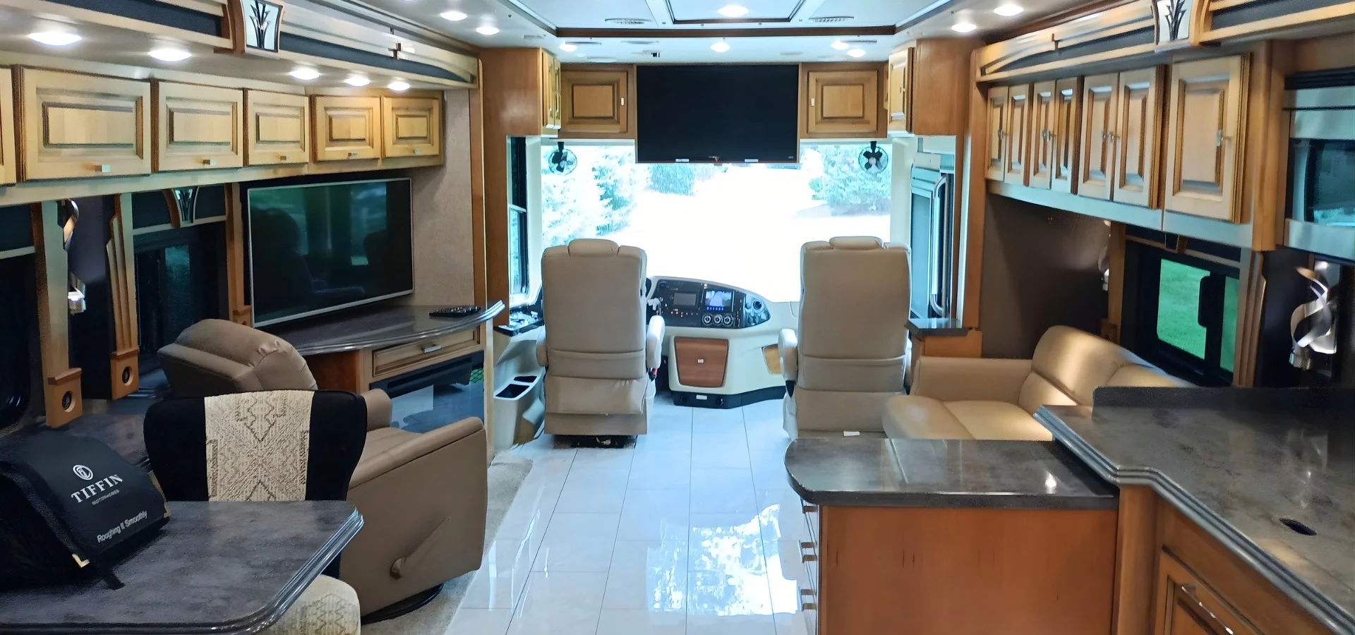 Luxurious motorcoach interior with leather seating, large TV, and wooden cabinets. Spacious layout for comfort during RV travels.