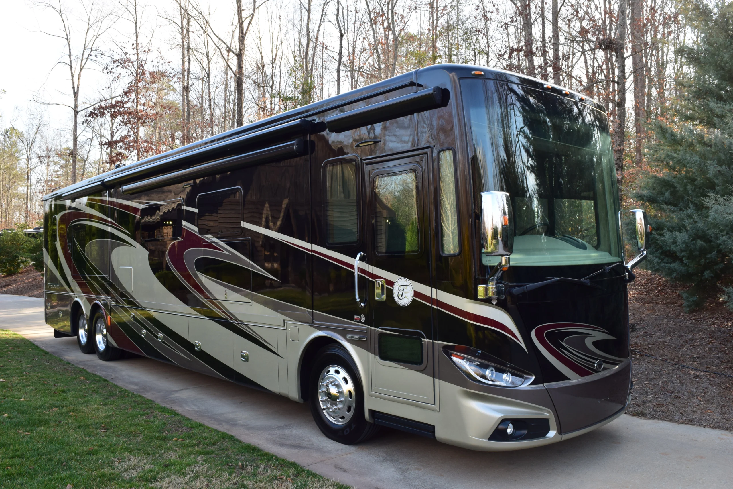 DSC_0391 Luxury motorcoach with glossy burgundy and gold swirls parked on a forested driveway.