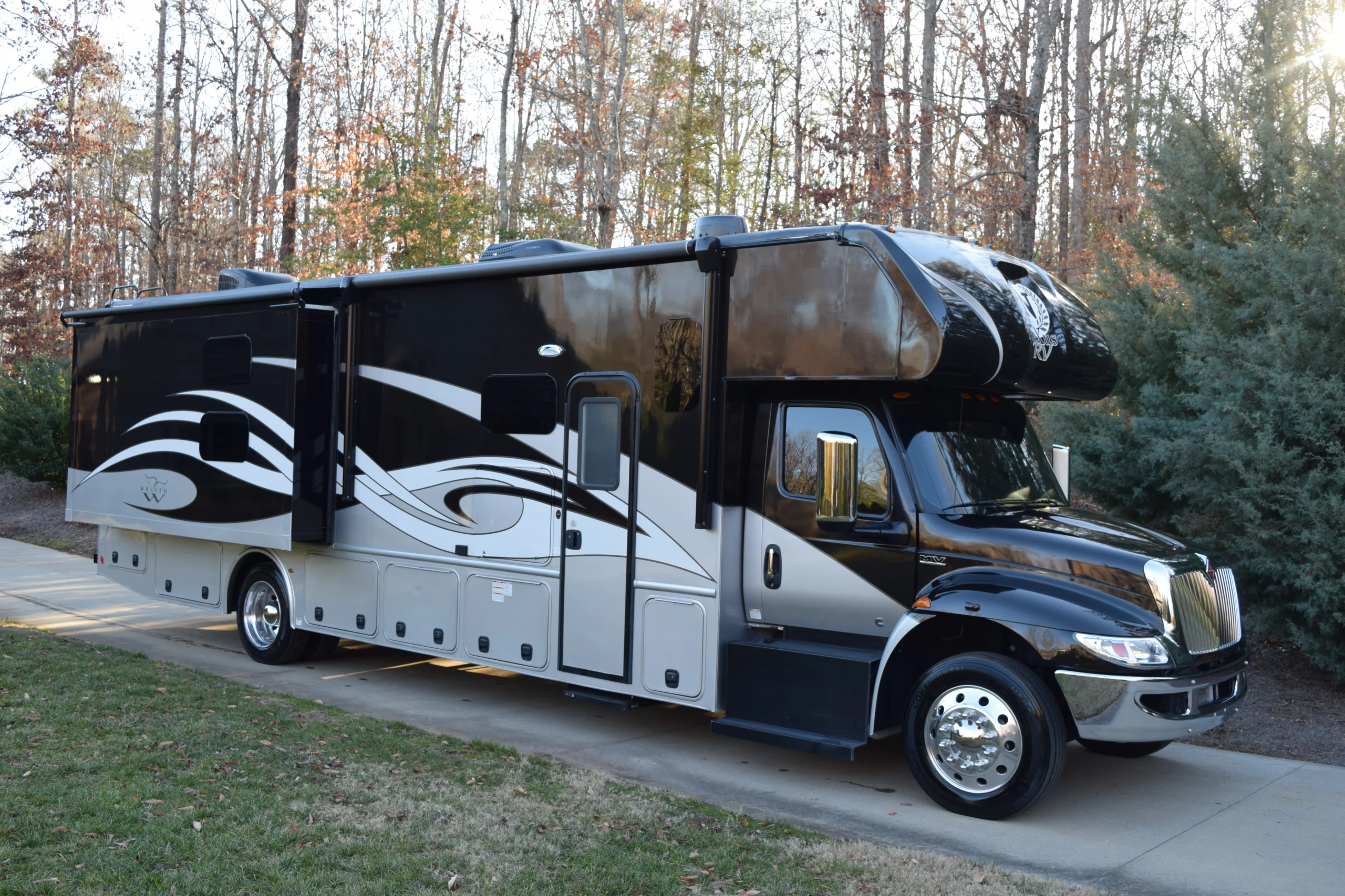 DSC_0001 Luxurious black and silver motorcoach parked on a driveway, surrounded by autumn trees.
