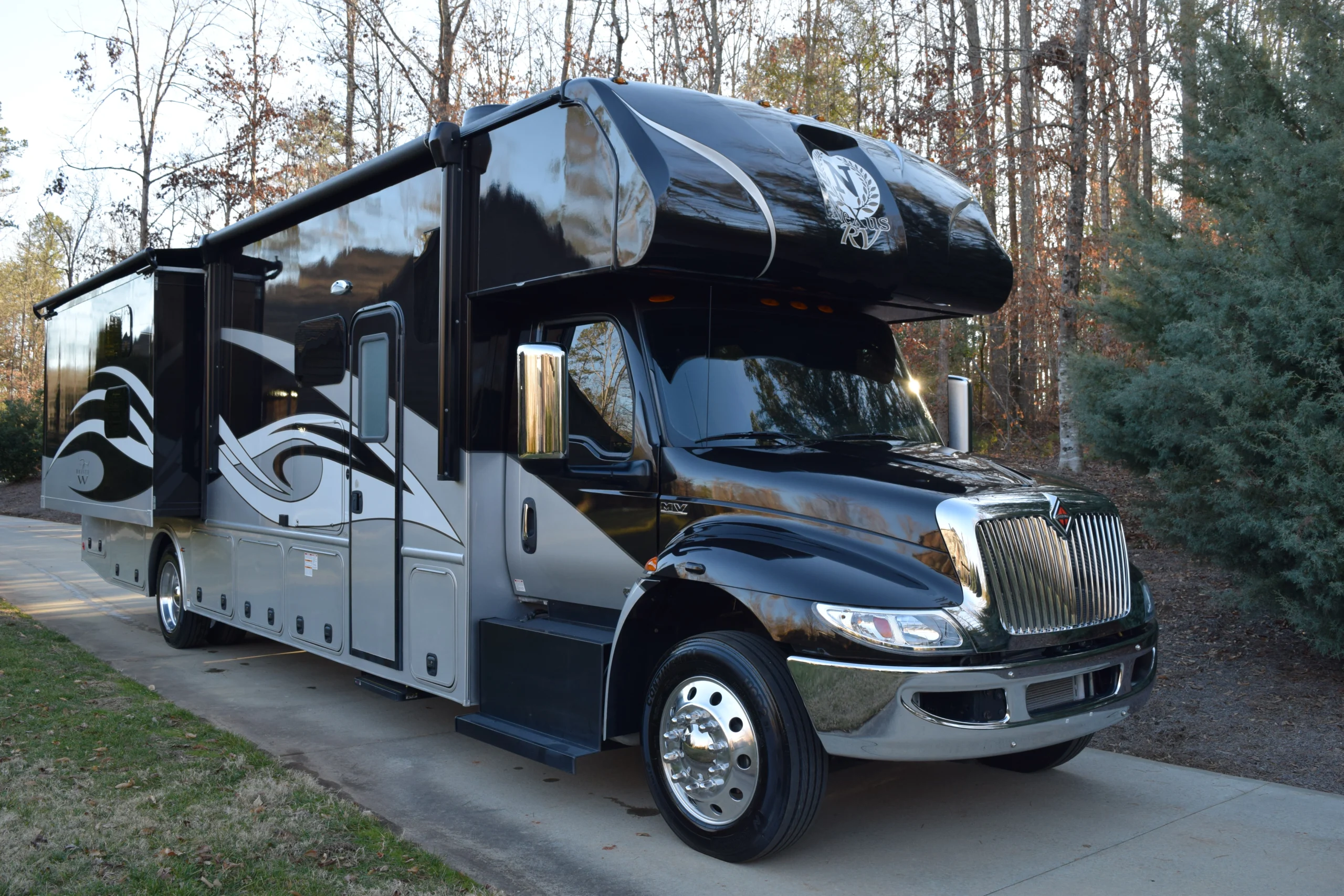 DSC_0004 Black and silver motorcoach with intricate designs parked on a driveway, surrounded by autumn trees.