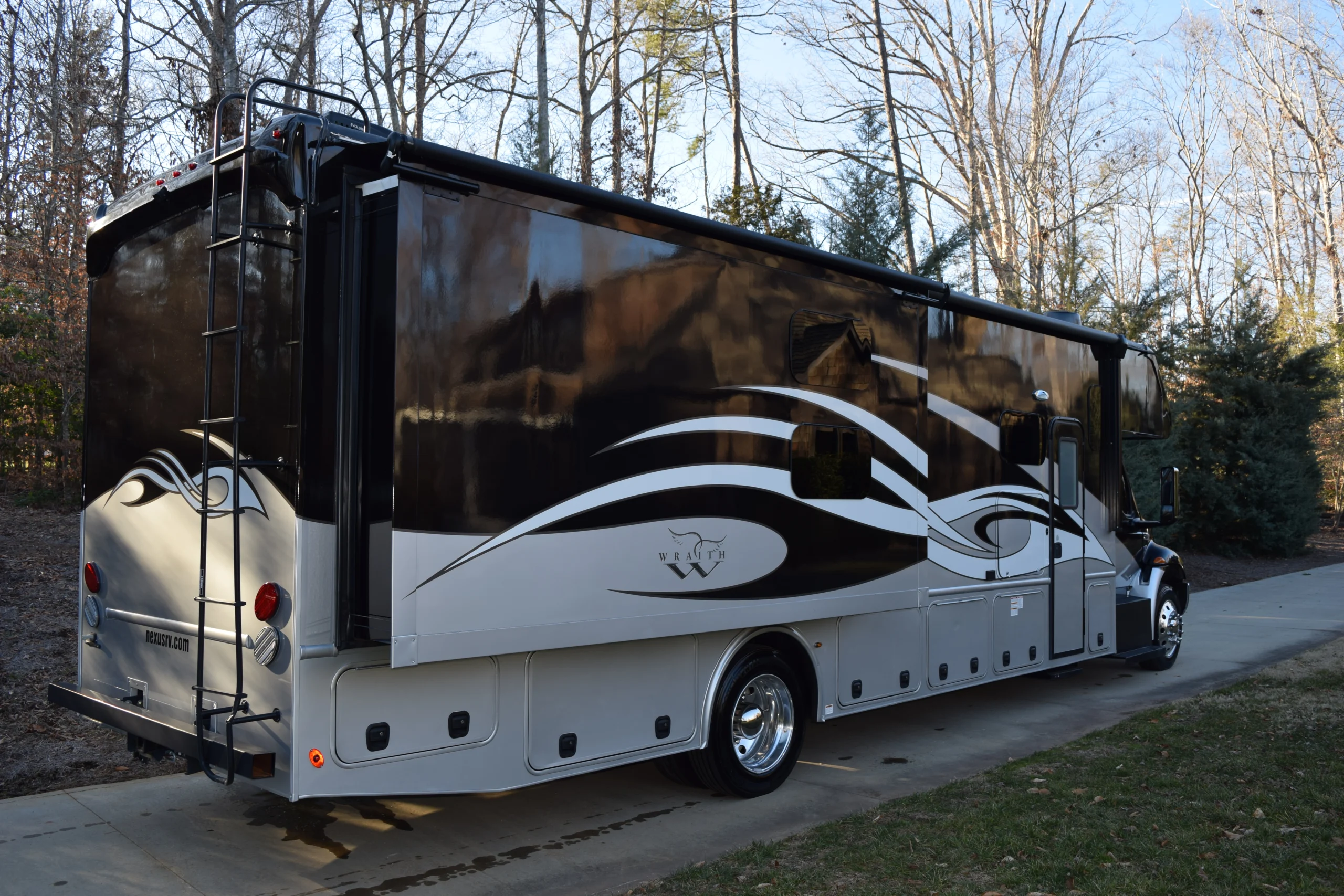 DSC_0007 Sleek black and white motorcoach parked on a driveway, surrounded by bare trees and greenery, featuring artistic swirl designs.
