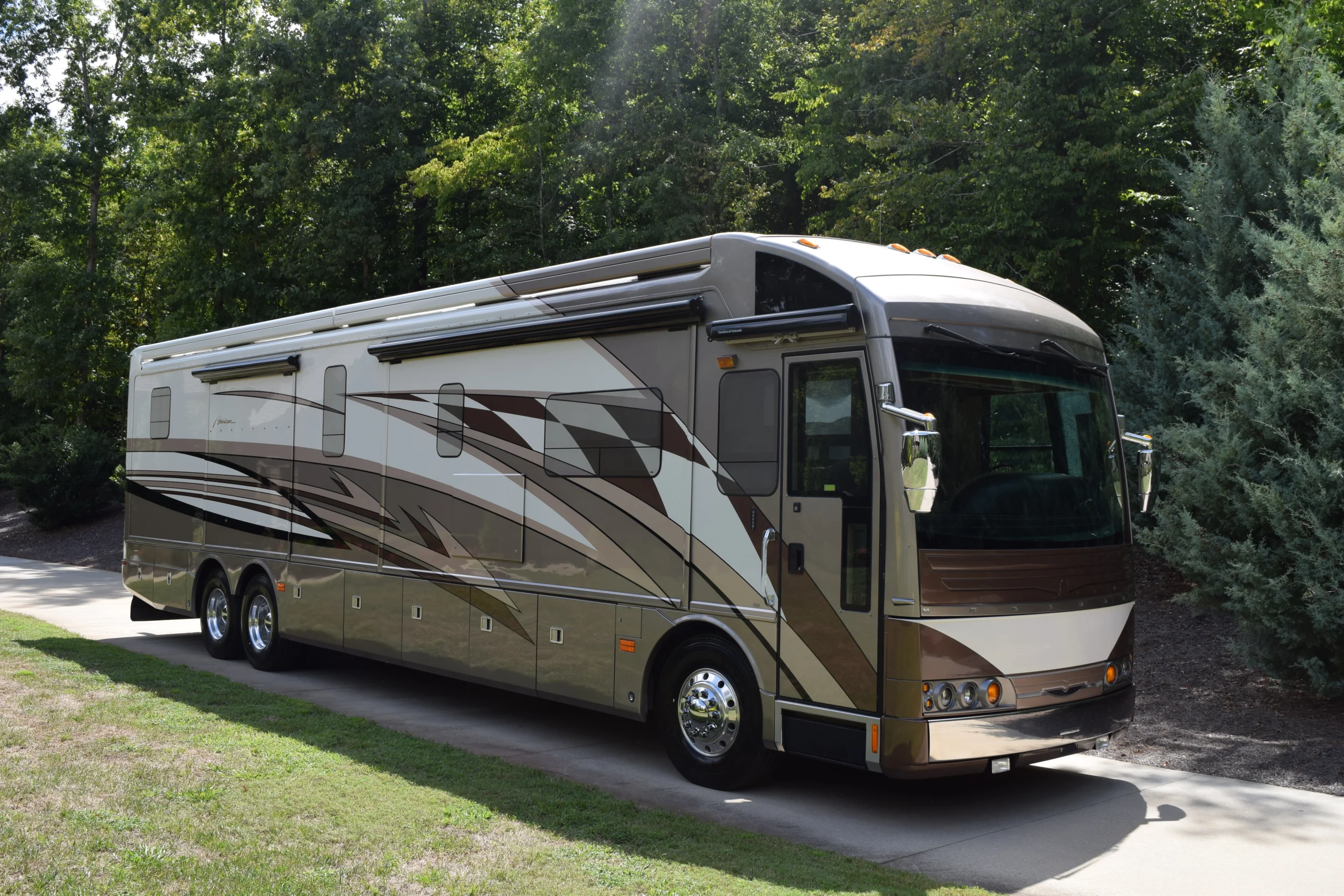 DSC_0035 Luxurious motorcoach parked on a driveway, surrounded by lush greenery, showcasing sleek design and metallic accents.