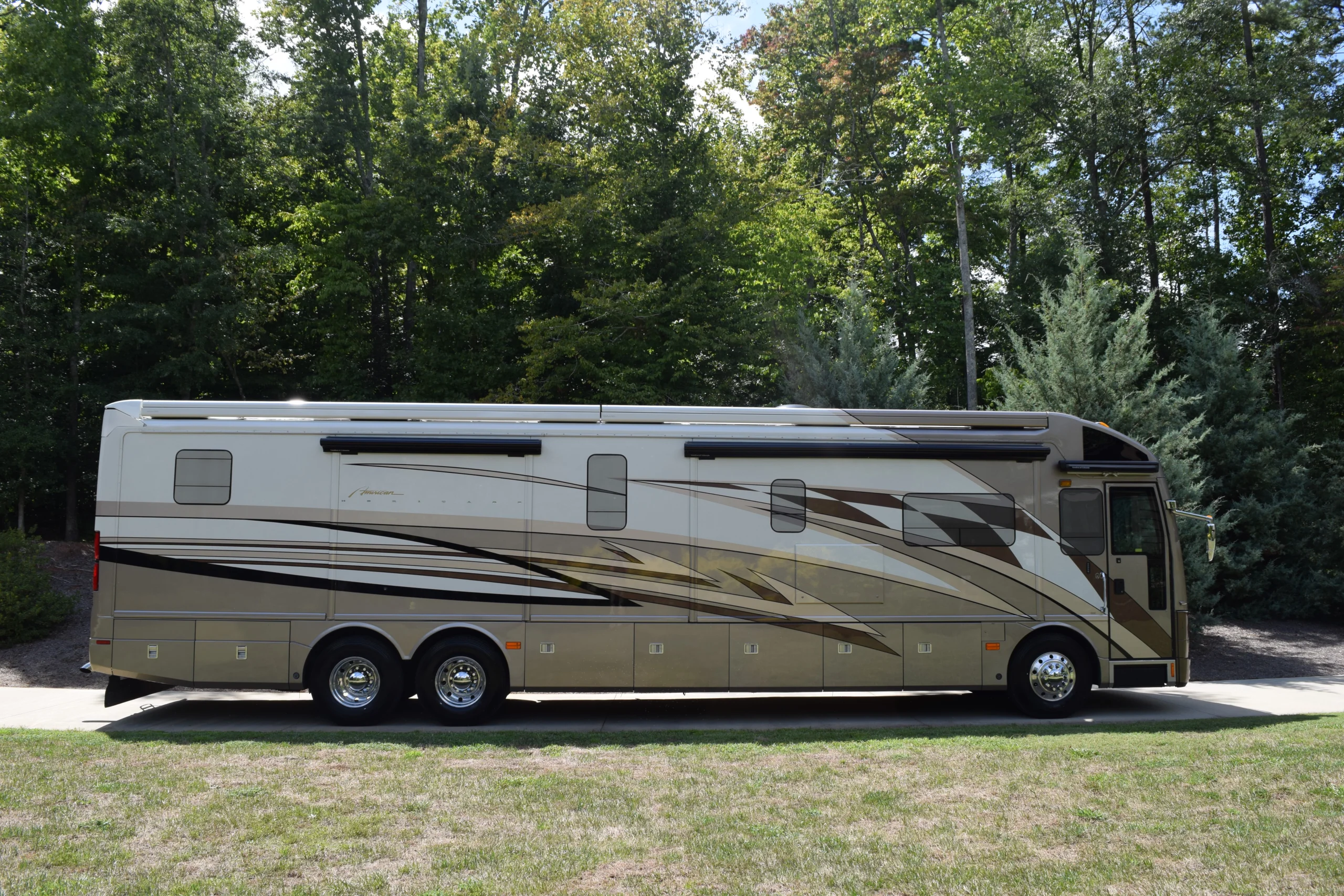 DSC_0039 Luxury Motorcoach parked on a driveway, surrounded by lush green trees and grass.