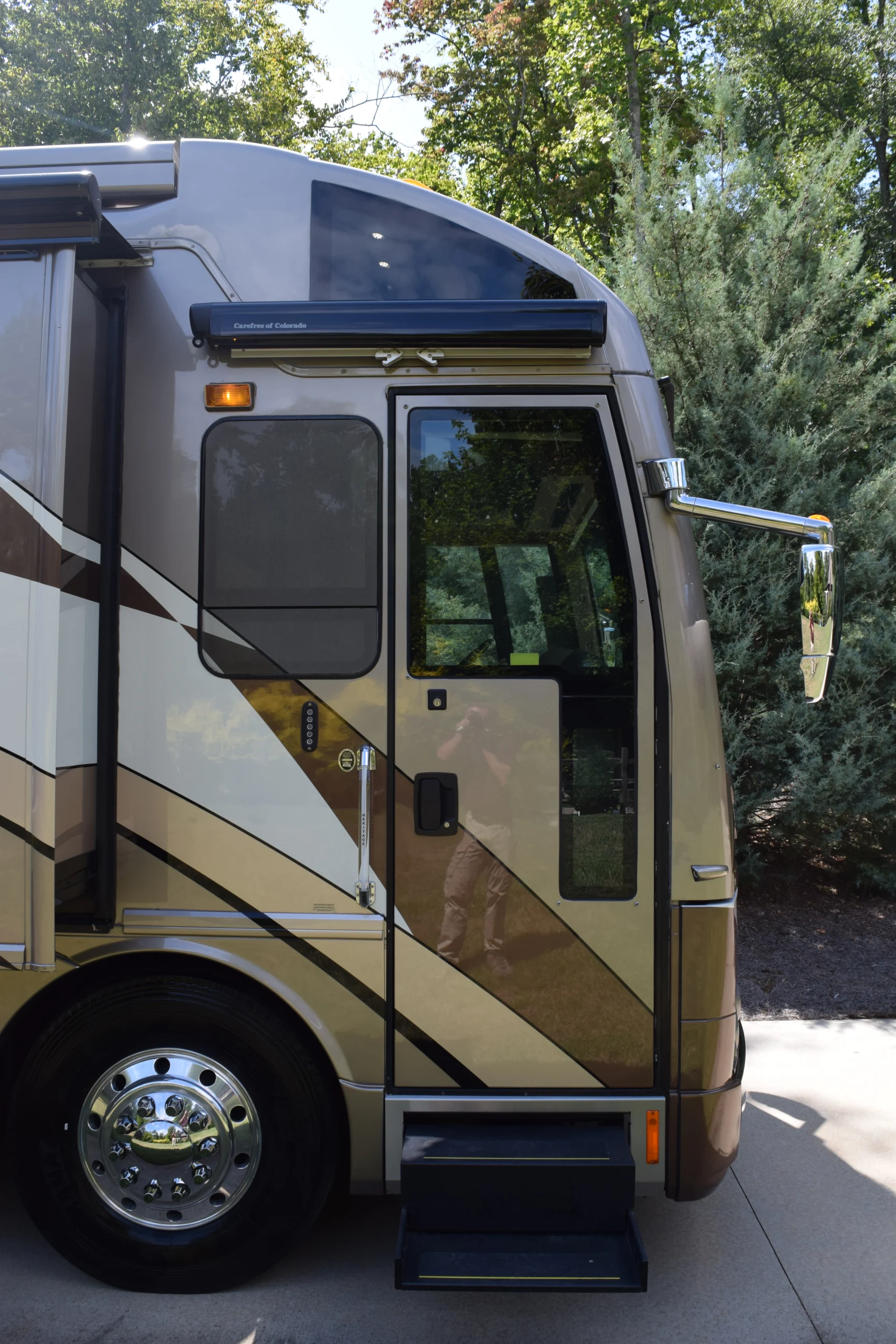 DSC_0041 The side entrance of a luxury motorcoach with retracted steps and reflective windows, surrounded by greenery.