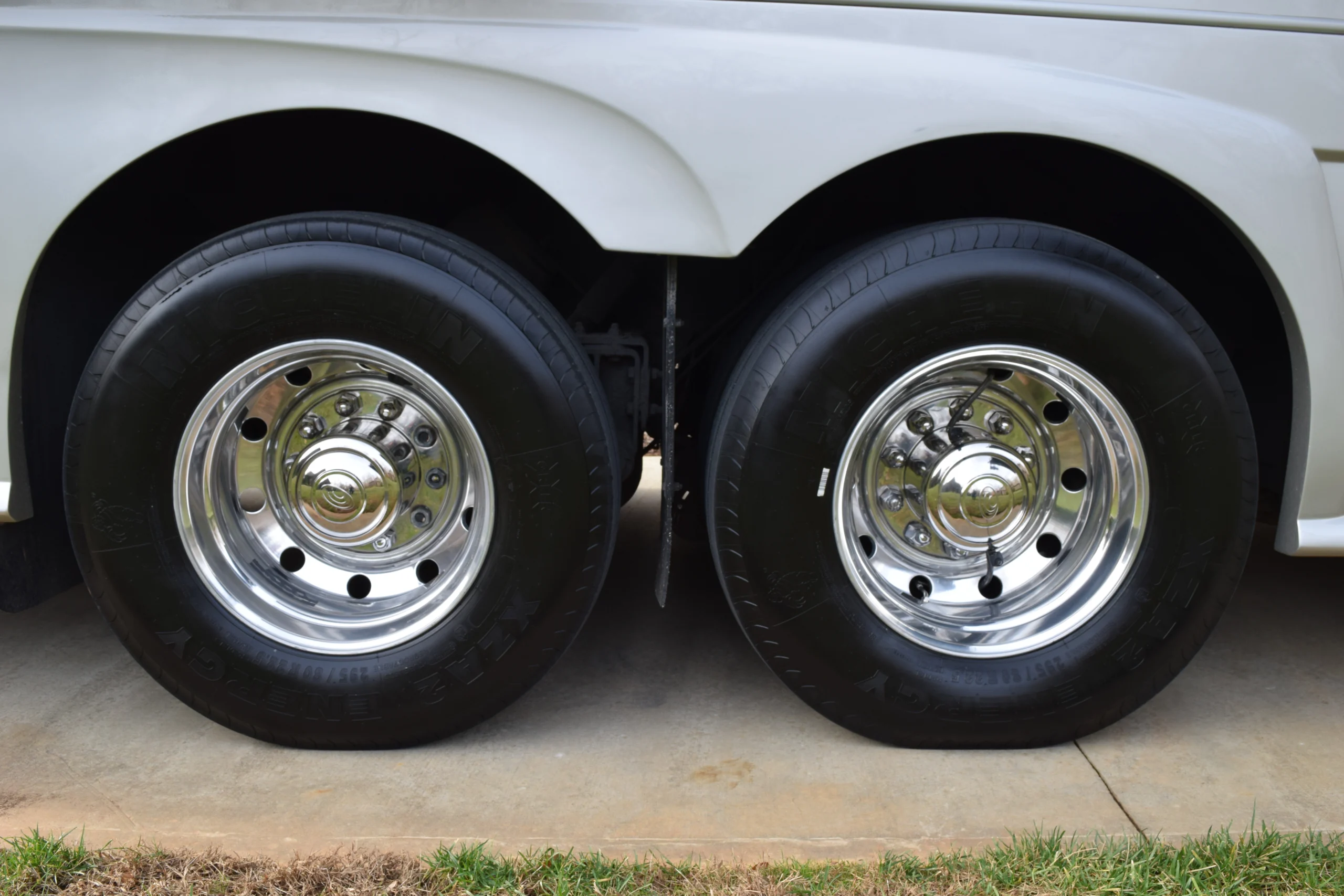 DSC_0158 Dual chrome wheels with black tires on a Motorcoach and RVs chassis, parked on concrete.
