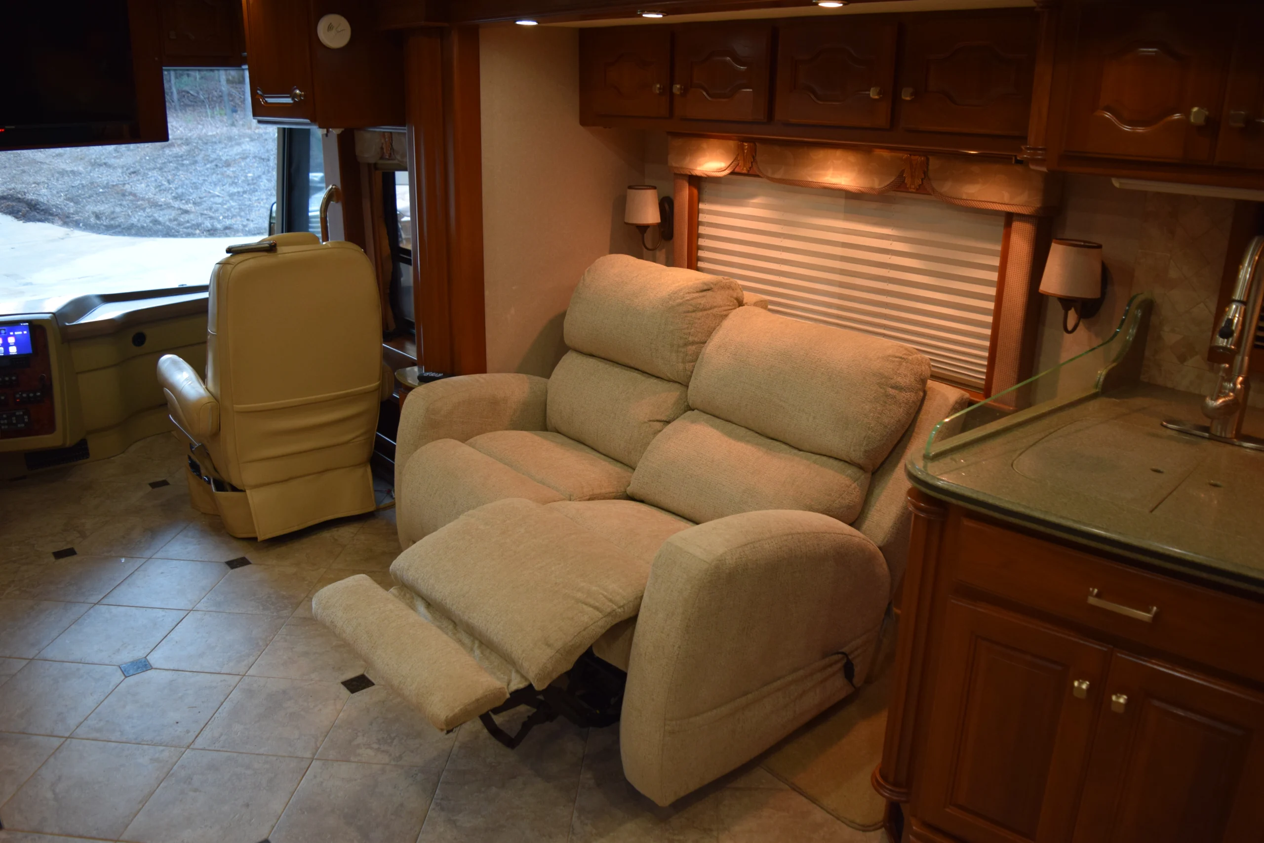 DSC_0174 Cozy RV interior with plush reclining sofa, leather captain's chair, and kitchen area, highlighting luxury in motorcoach and RVs.
