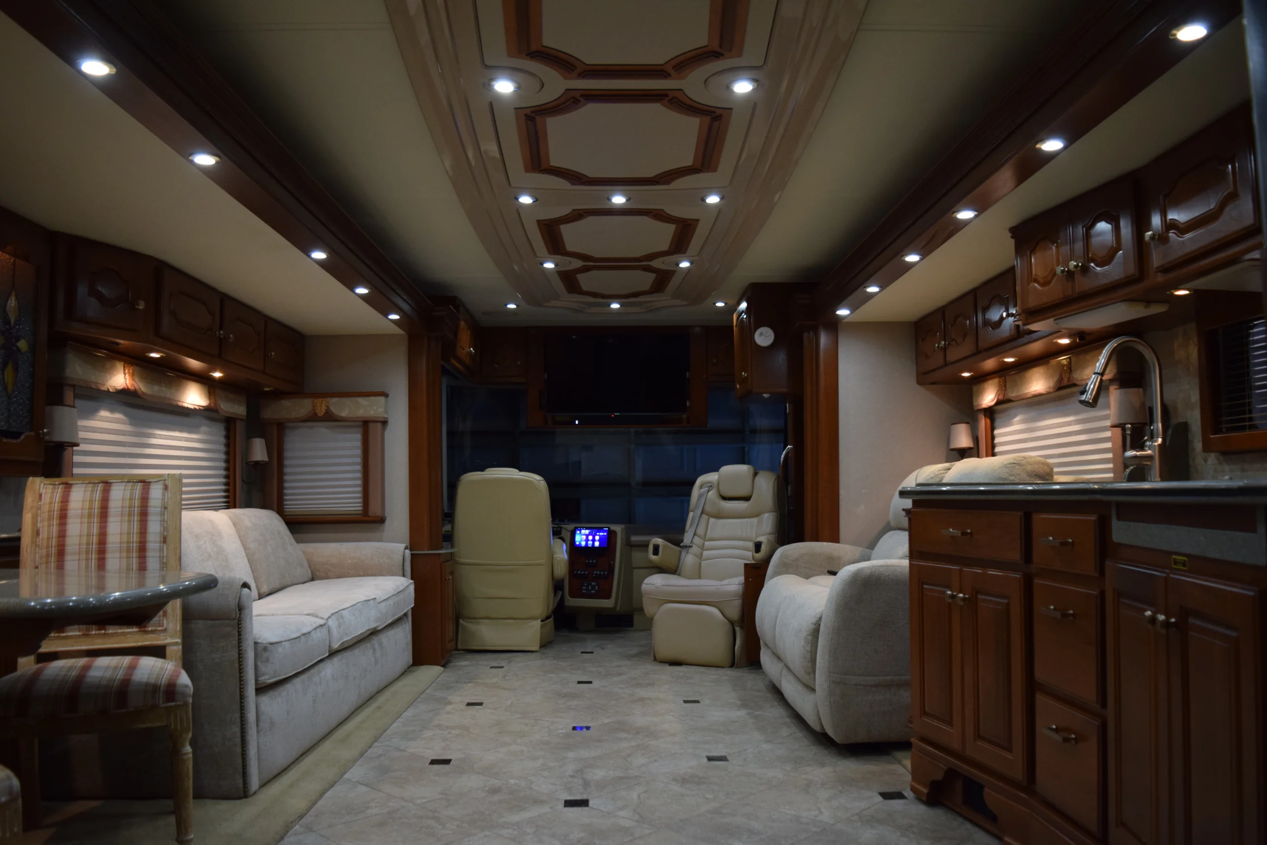 DSC_0207 Luxurious motorcoach interior, featuring plush seating, wooden cabinetry, modern lighting, and a compact kitchen area, ideal for RV enthusiasts.