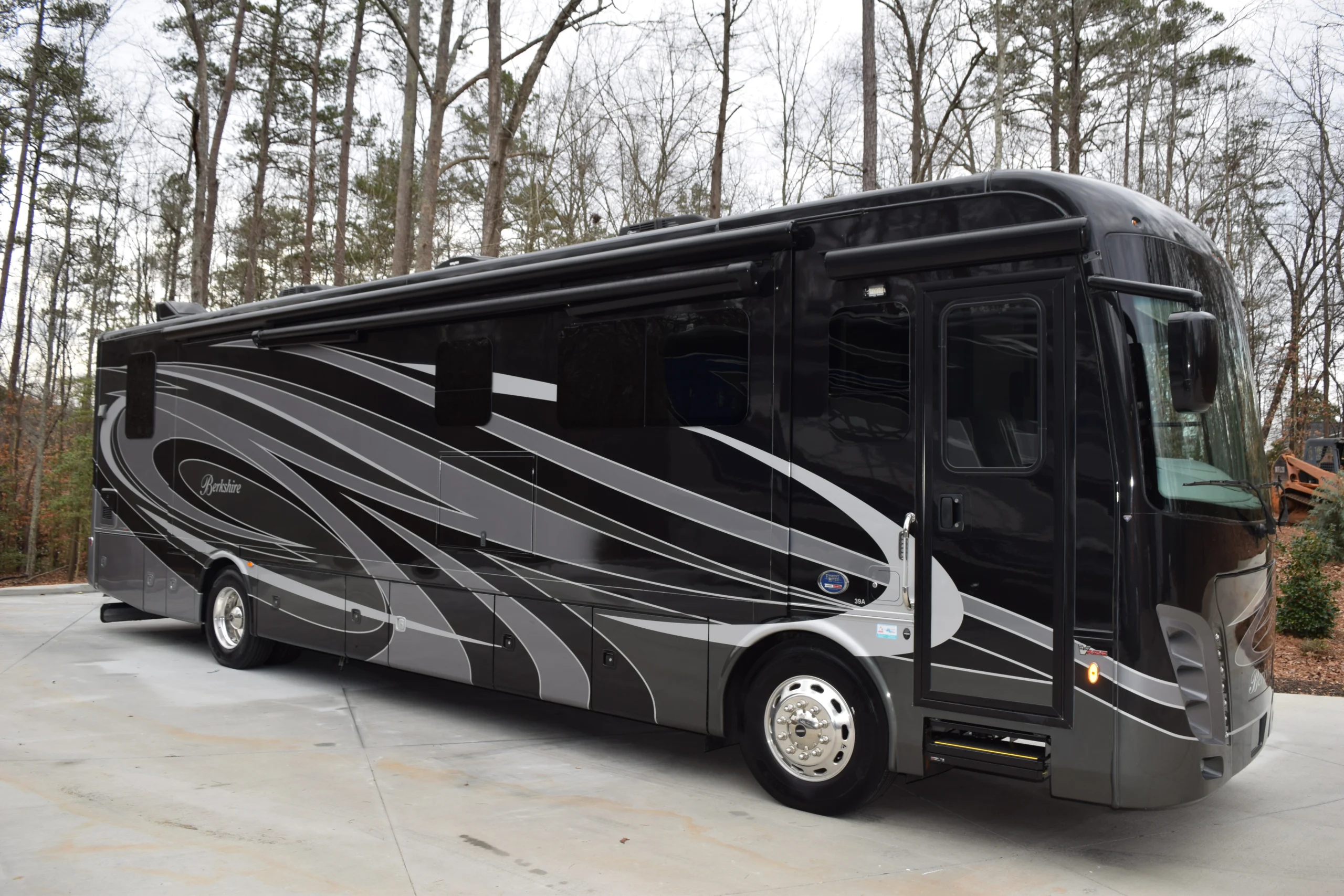 DSC_0241 Luxurious black and gray motorcoach with sleek design parked in a wooded area, featuring large windows and a streamlined body.