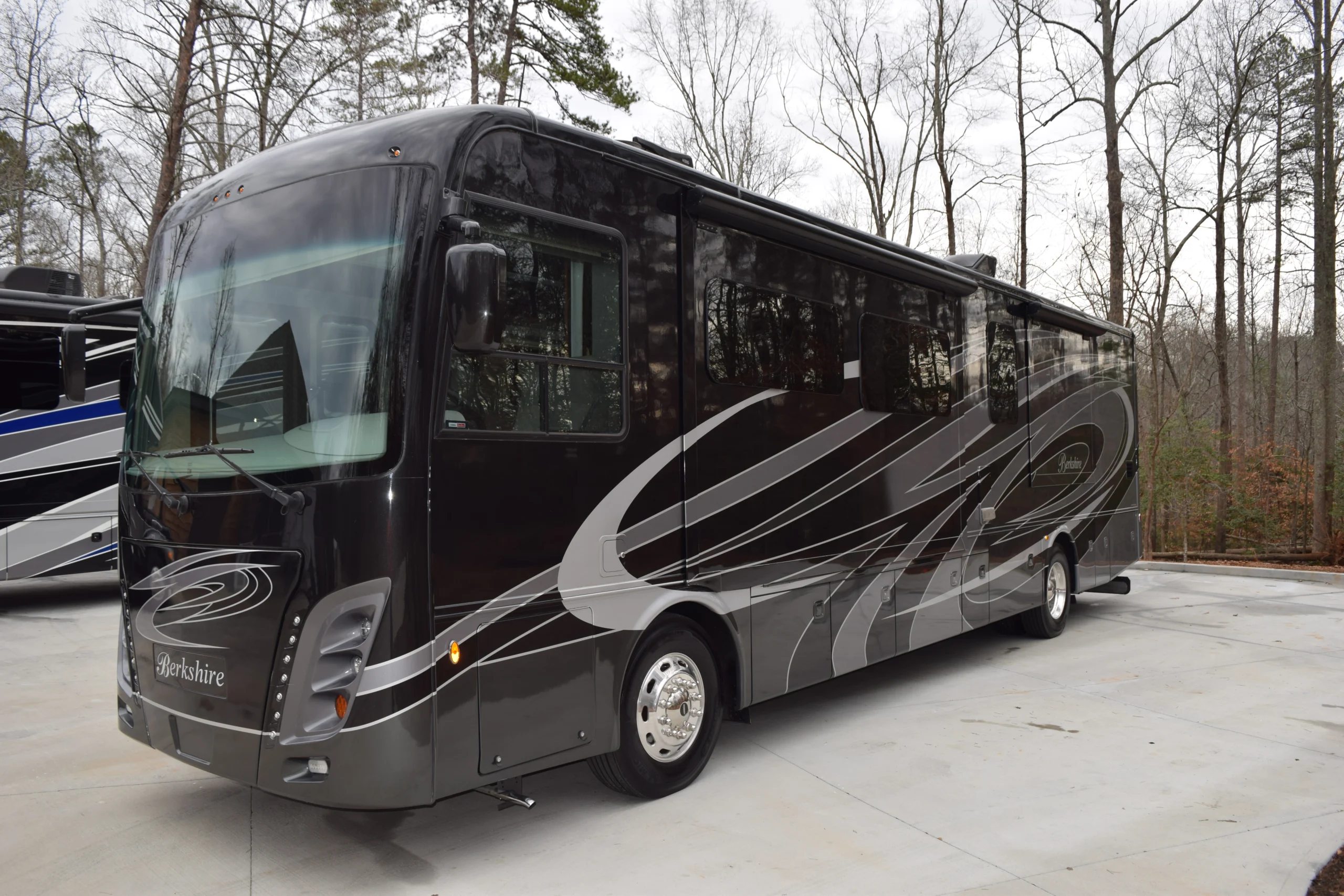 DSC_0251 Luxurious Berkshire motorcoach with sleek black and silver design, parked on a wooded driveway.