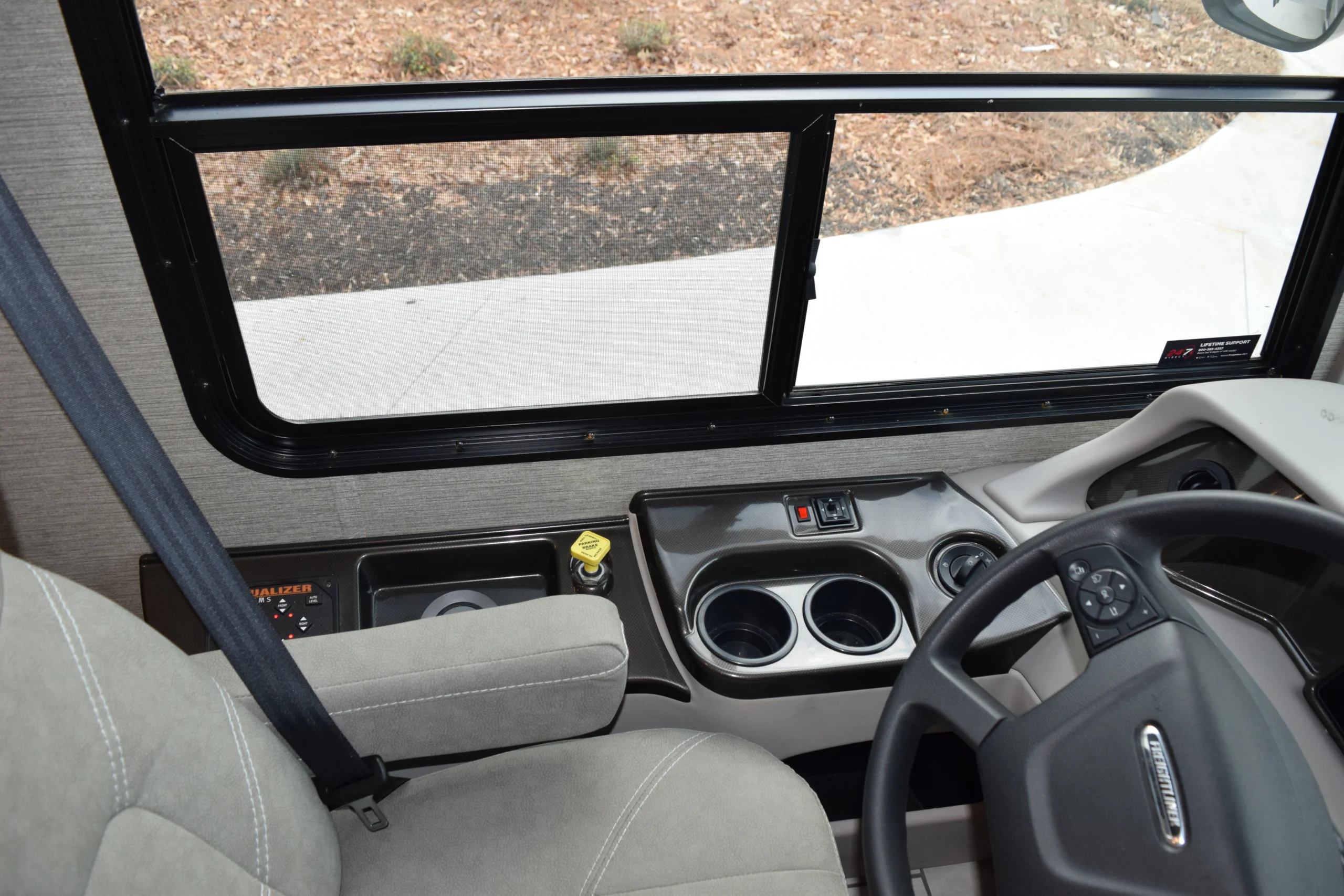 DSC_0290 Motorcoach interior showing driver's seat, steering wheel, and dashboard console with cup holders and control buttons.