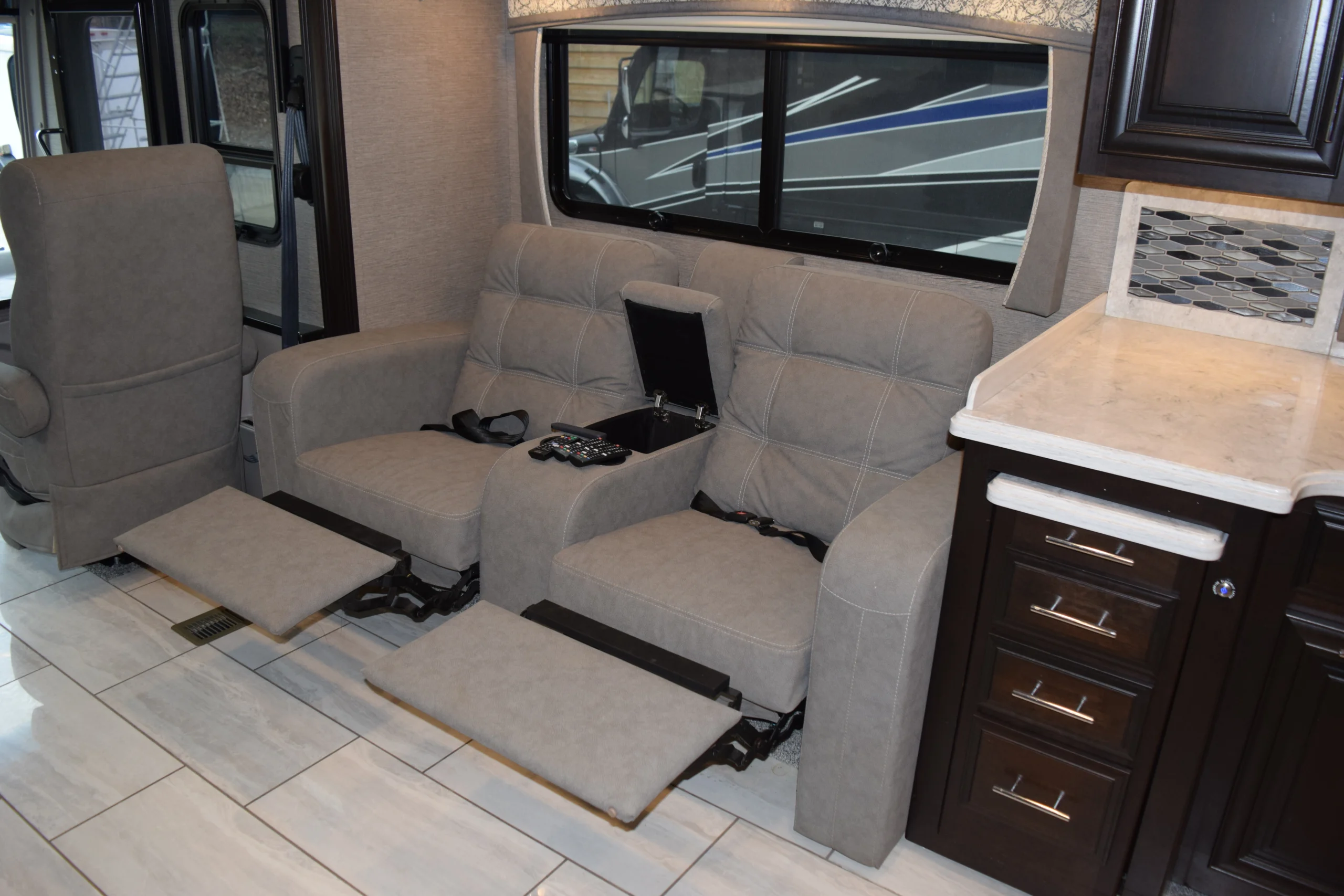 DSC_0296 Gray recliners with footrests, remote controls on center console in a sleek, modern Motorcoach and RVs interior.