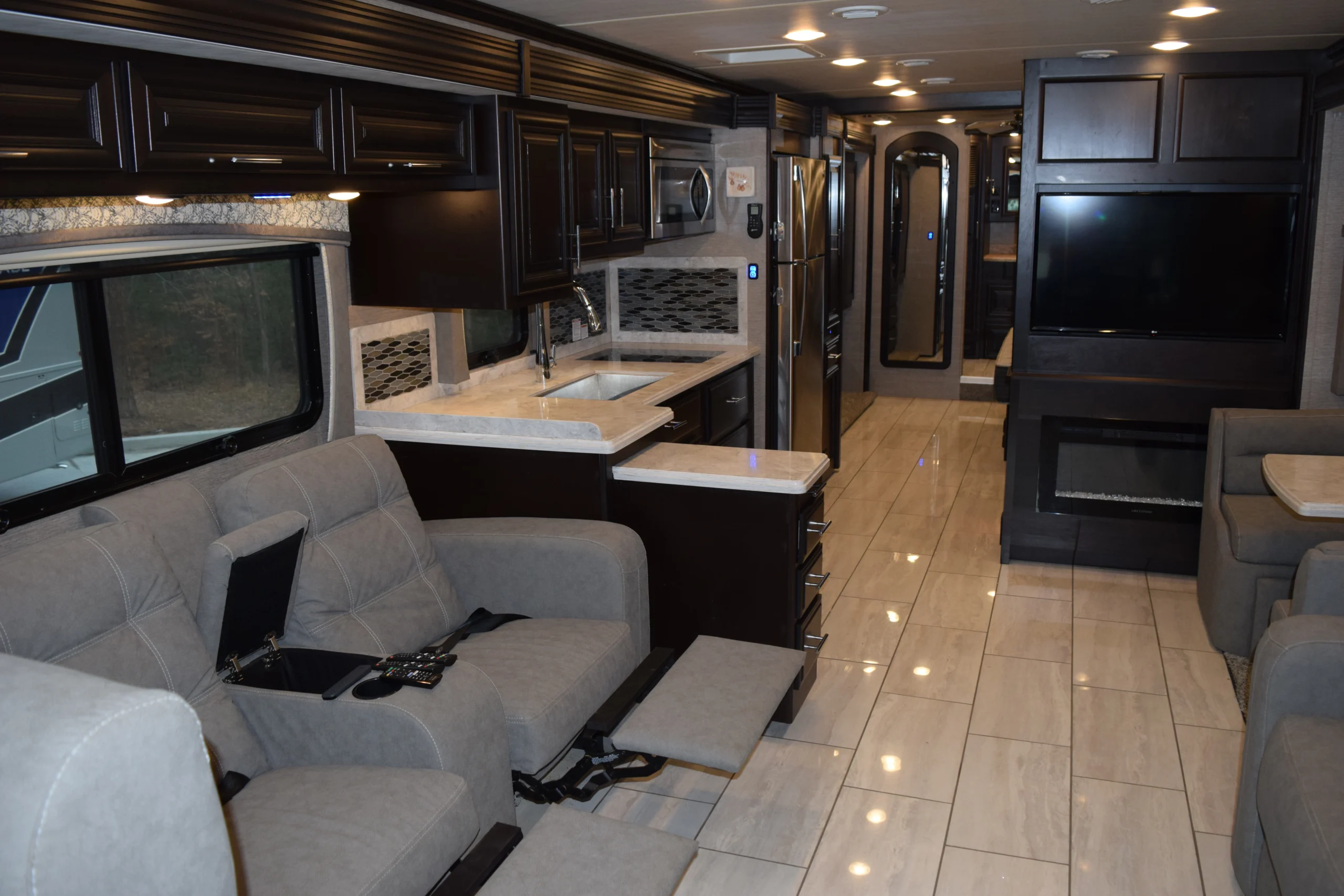 DSC_0299 Luxurious Motorcoach and RVs interior with beige recliners, modern kitchen, stainless appliances, and flat-screen TV.