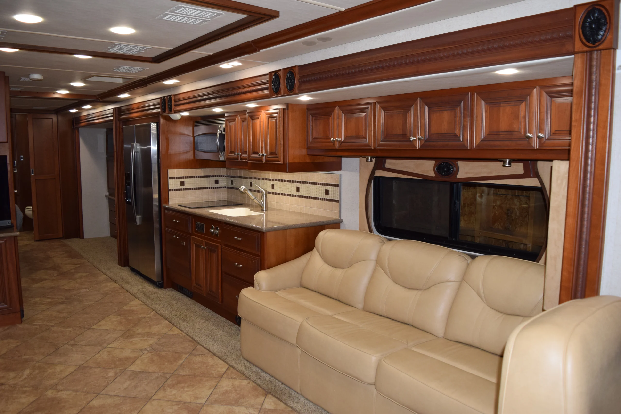 DSC_0332 Luxurious Motorcoach and RVs interior with tan leather sofa, wooden cabinets, stainless steel appliances, and tiled floor.