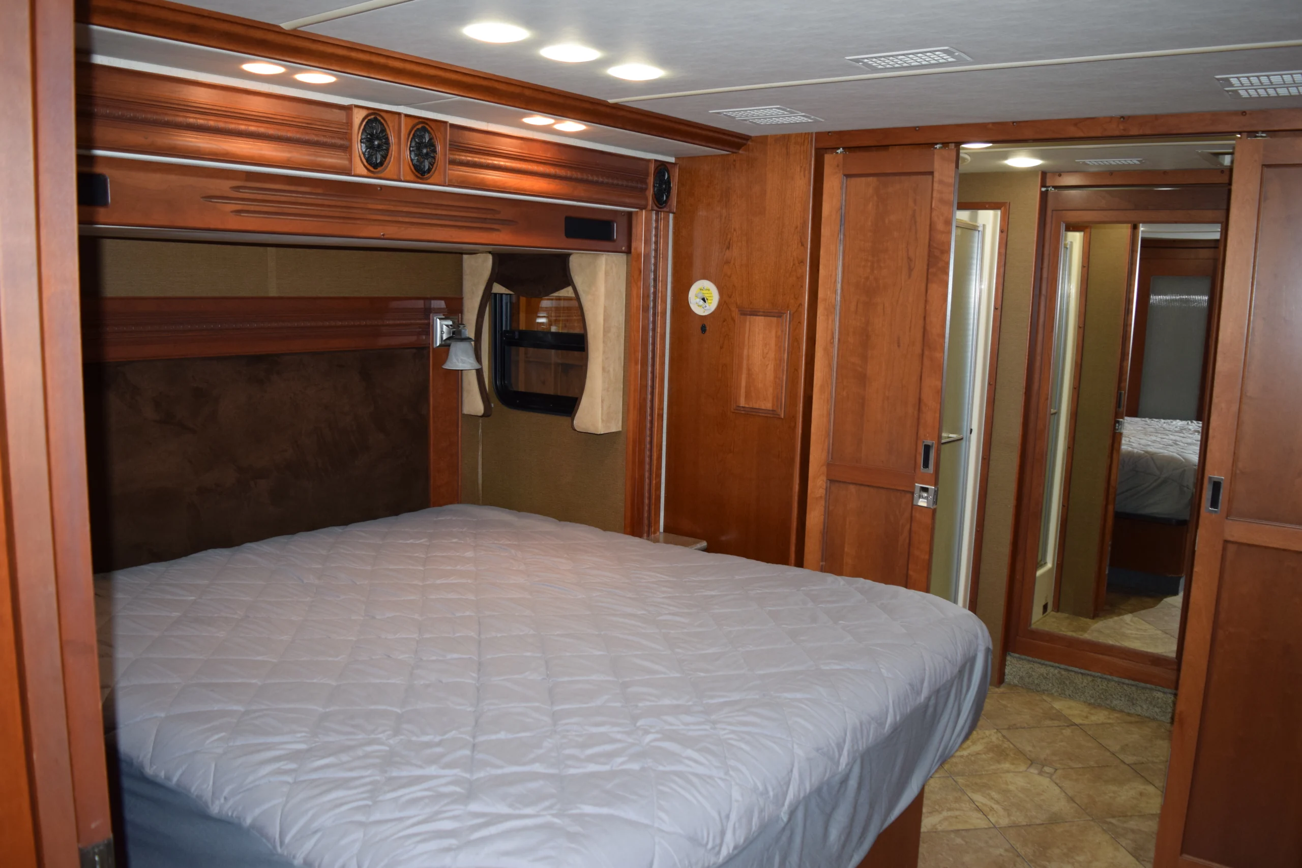 DSC_0336 Luxurious Motorcoach and RVs interior with wood paneling, large bed, overhead lights, curtains, and mirrored sliding doors.