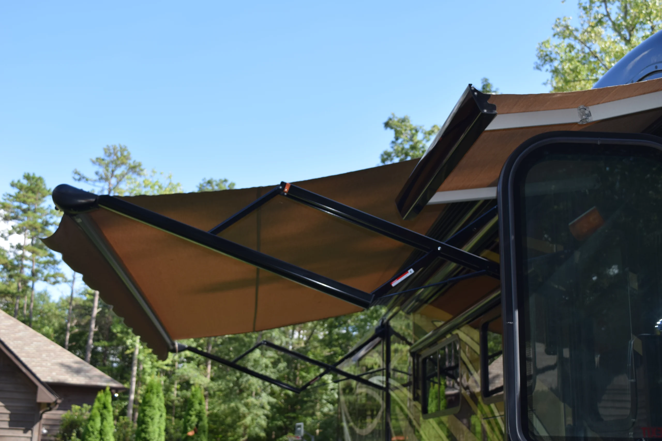 DSC_0349 Retractable awning extended from Motorcoach and RVs, shaded by trees and under a clear blue sky.