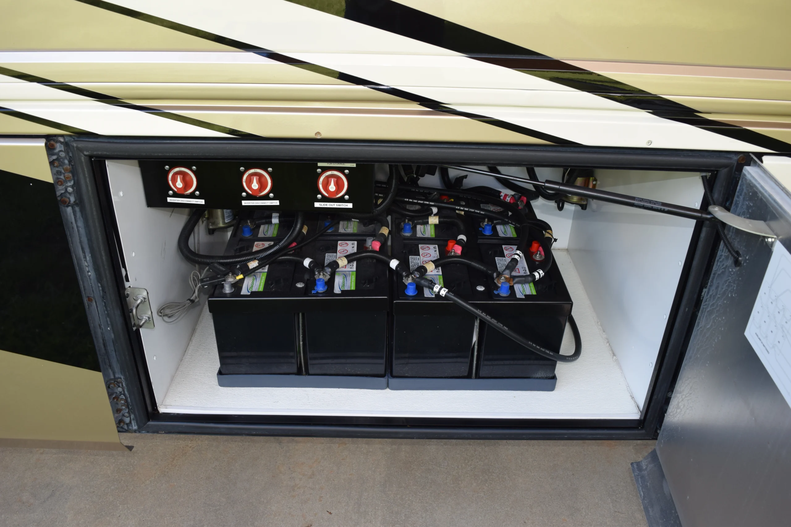 DSC_0351 Motorcoach and RVs battery compartment with four batteries and red power switches, cables labeled and organized inside a secure compartment.